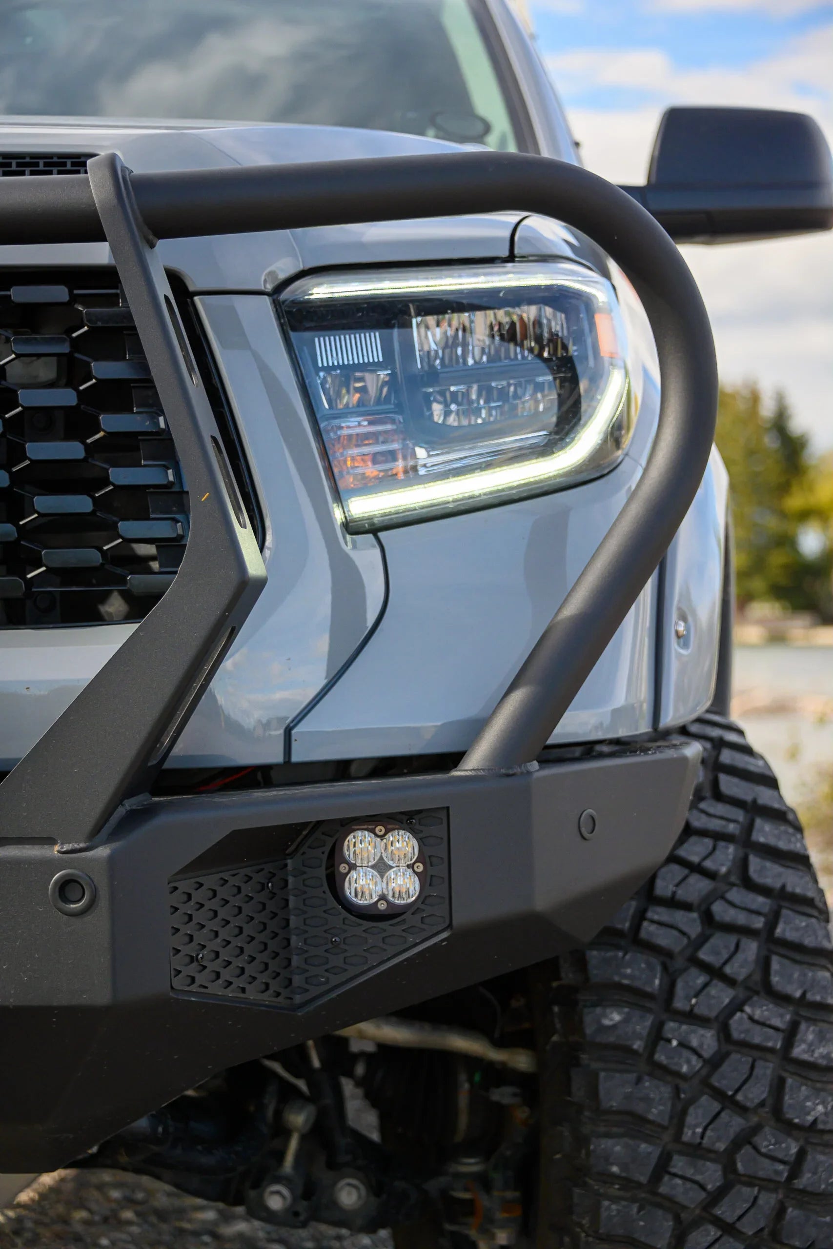 Close-up of off-road vehicle front bumper with grille guard, LED fog lights, and rugged tire
