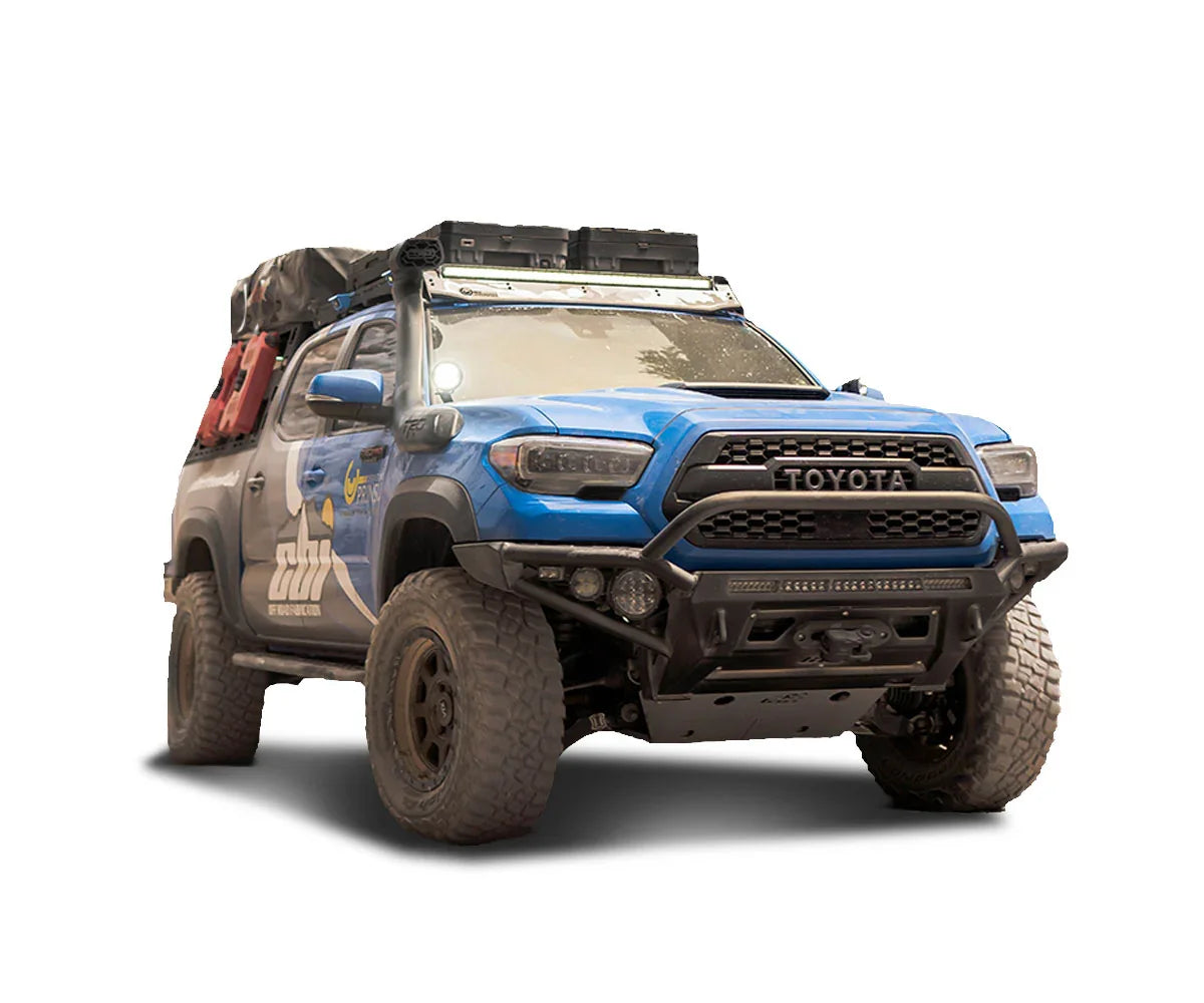 Blue Toyota Tacoma overland truck with roof rack, off-road tires, and camping gear