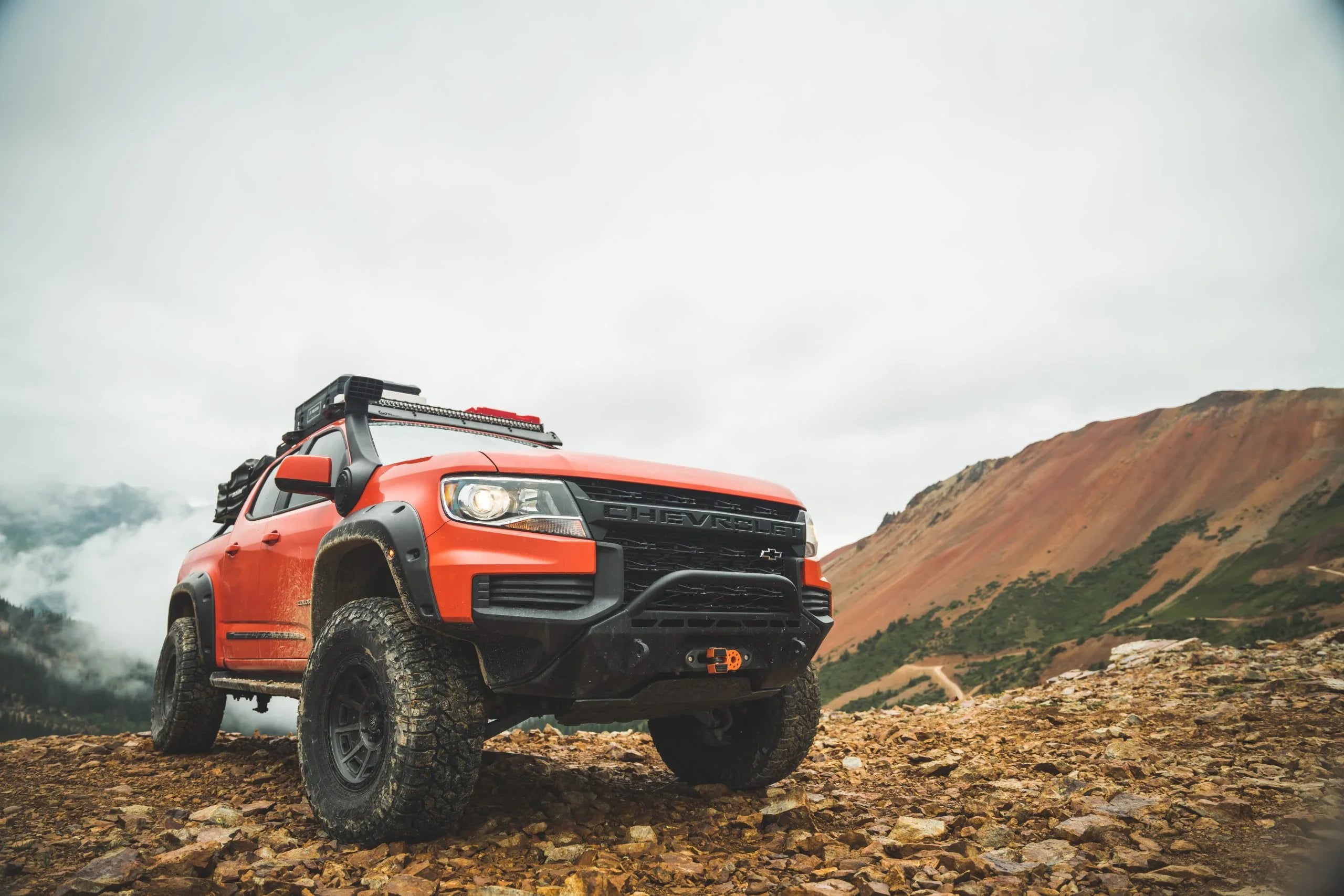 Lifted red Chevrolet overland truck with off-road tires and gear in a rocky mountain landscape