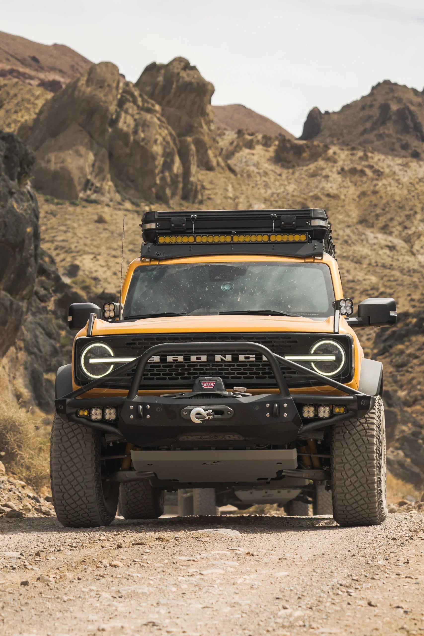 Yellow Ford Bronco with off-road gear and roof rack driving on rocky desert trail