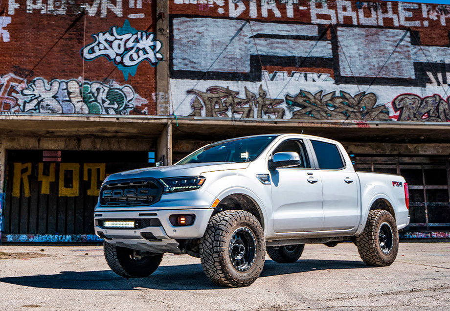 Lifted white Ford Ranger pickup truck with off-road tires parked in front of graffiti wall