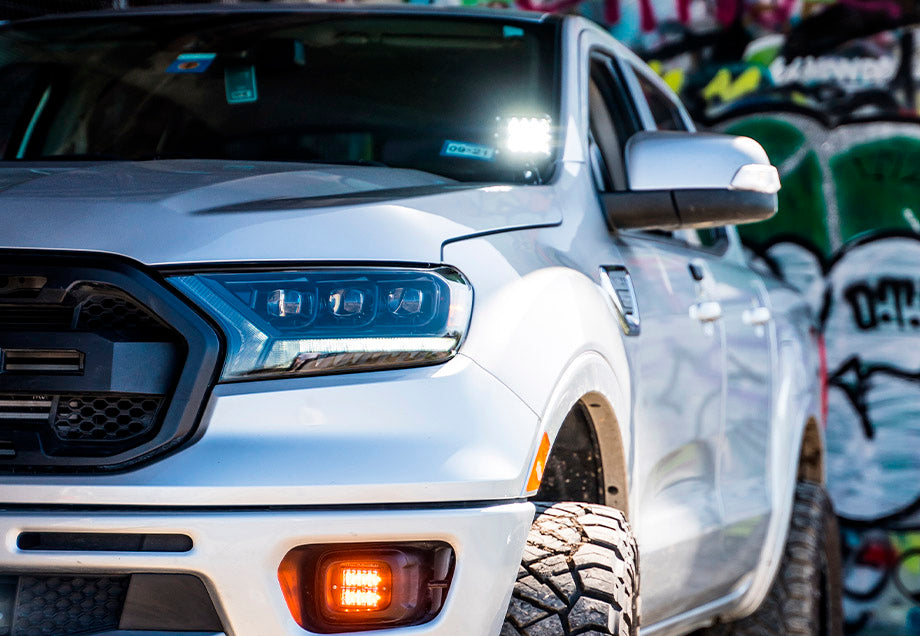 Close-up of silver off-road truck with rugged tires and LED lights, graffiti wall background