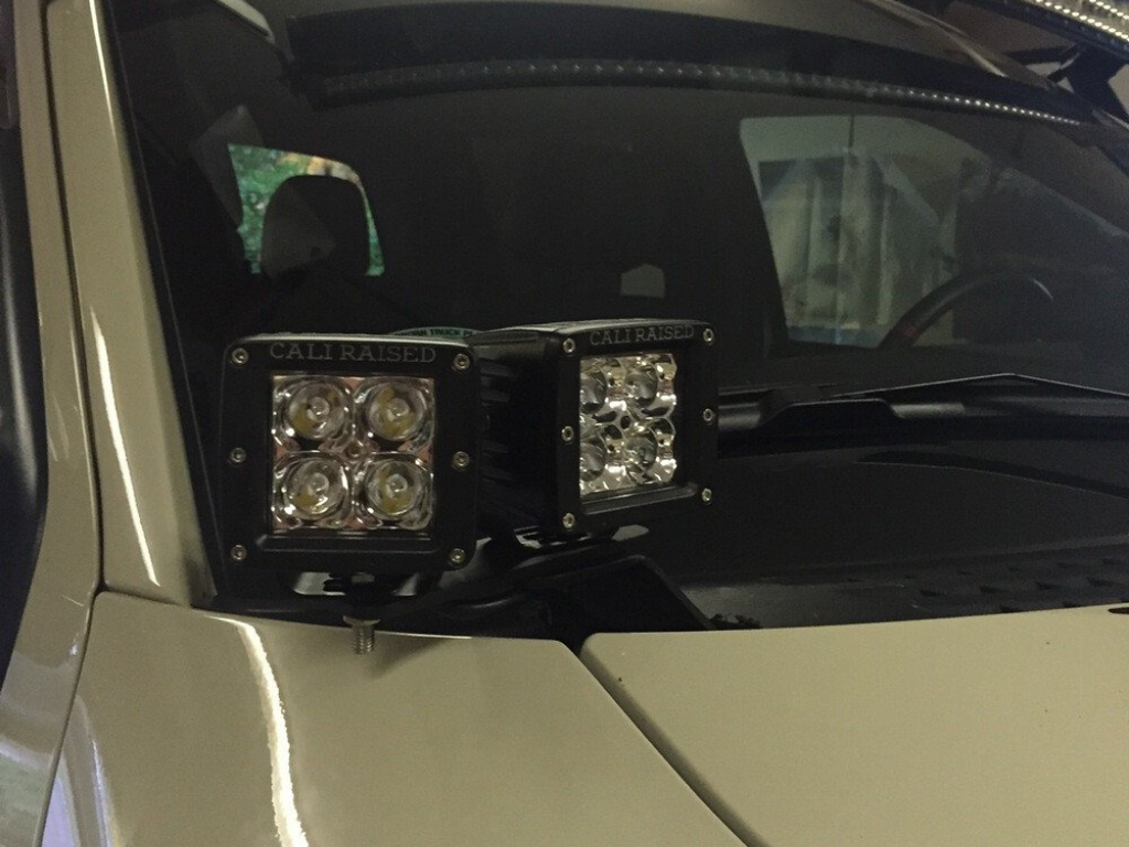 Ditch light bracket extensions mounted on vehicle hood with LED cube lights, close-up view