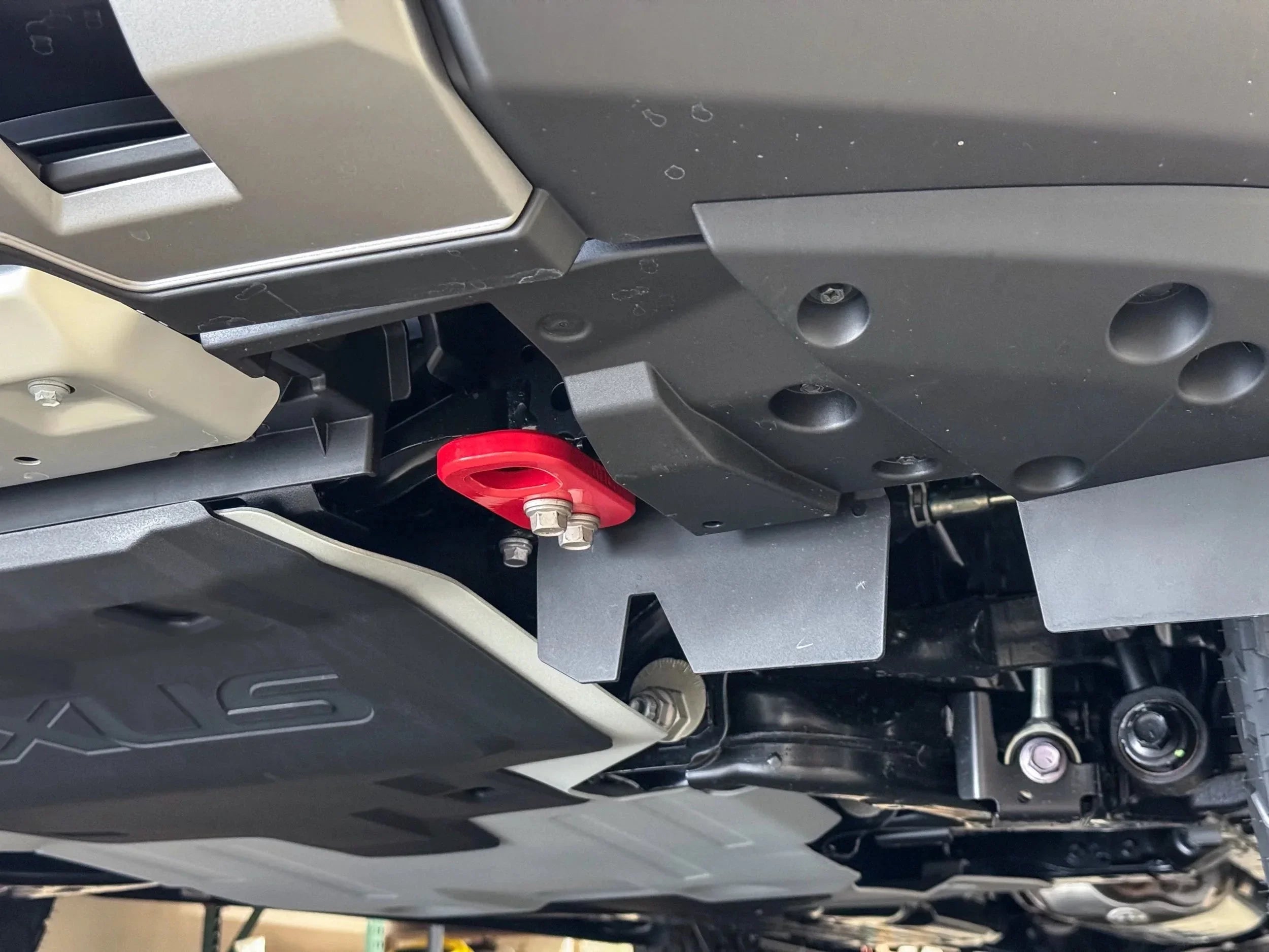 Close-up of red recovery point and skid plates under off-road vehicle chassis