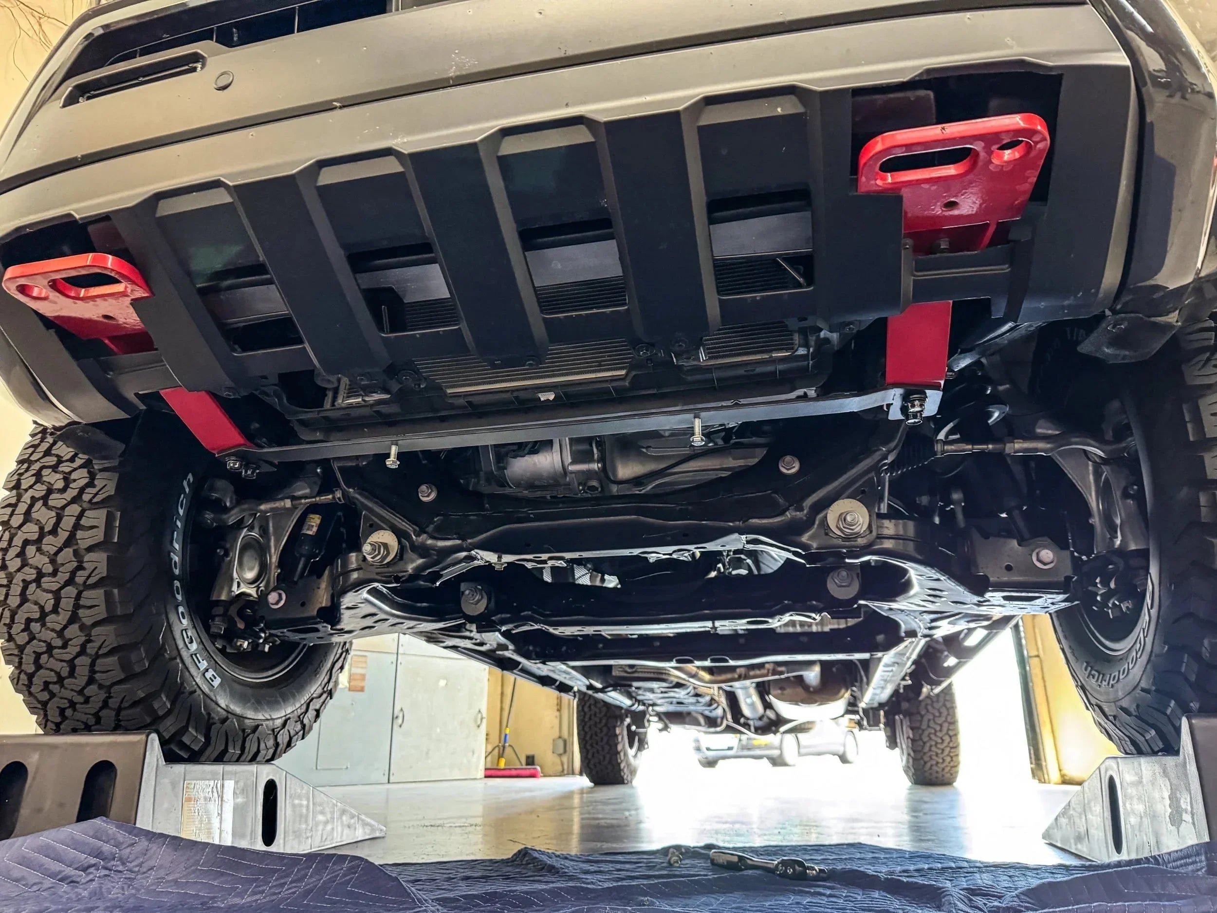 Undercarriage view of off-road vehicle with skid plate, lifted suspension, and red tow hooks