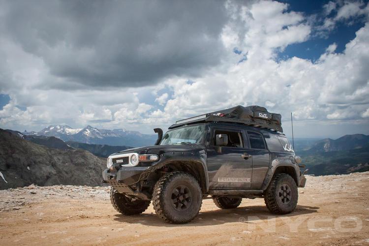 Toyota FJ Cruiser with roof rack and off-road gear on a mountain trail, rugged terrain adventure