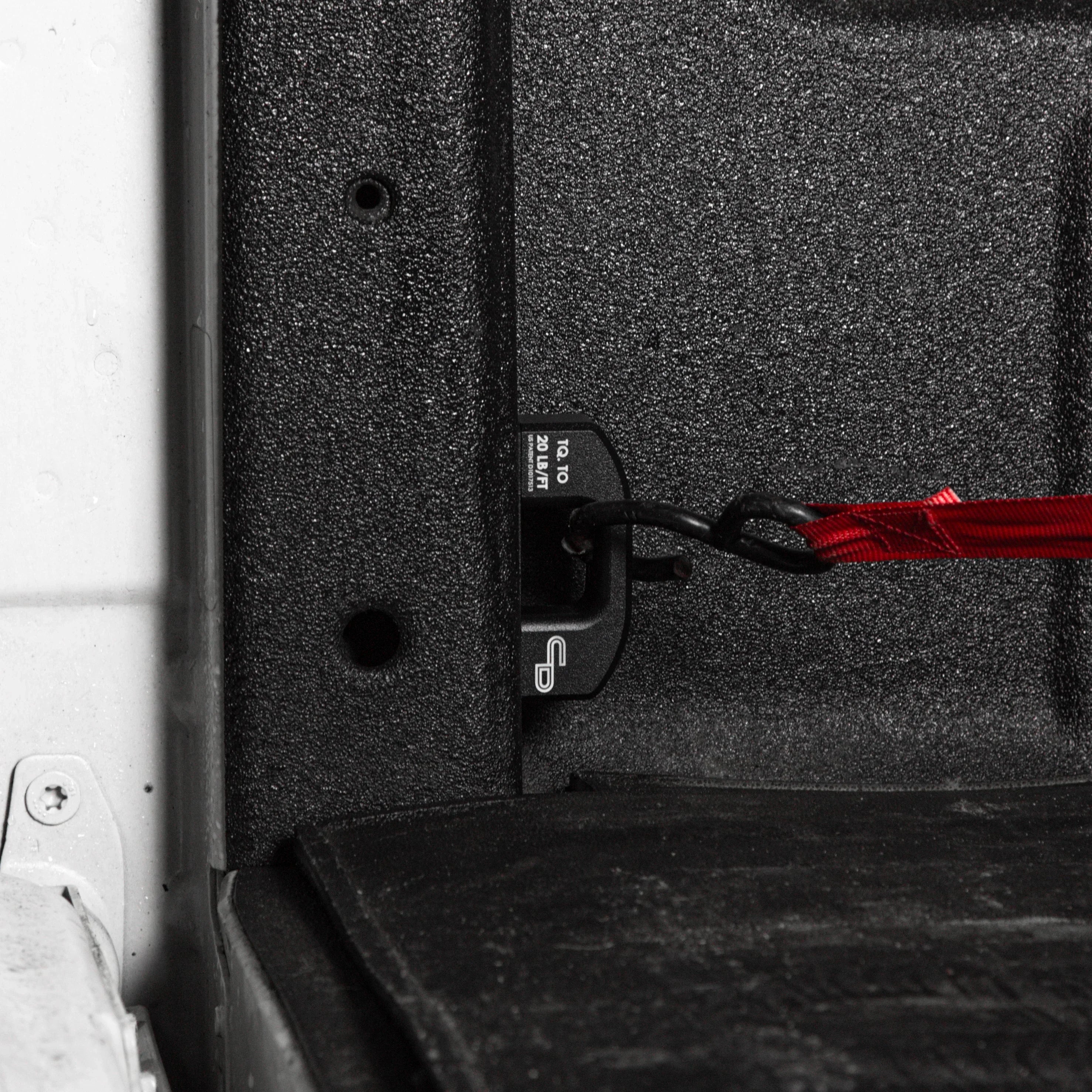 Black bed tie down anchor installed in Ford Super Duty truck bed with red strap attached