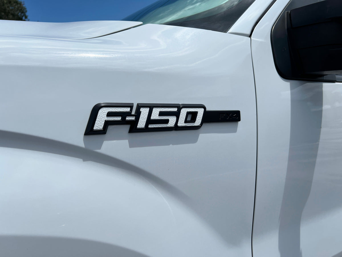 Black Tufskinz F-150 emblem insert on the front fender of a white 2009-2014 Ford F-150