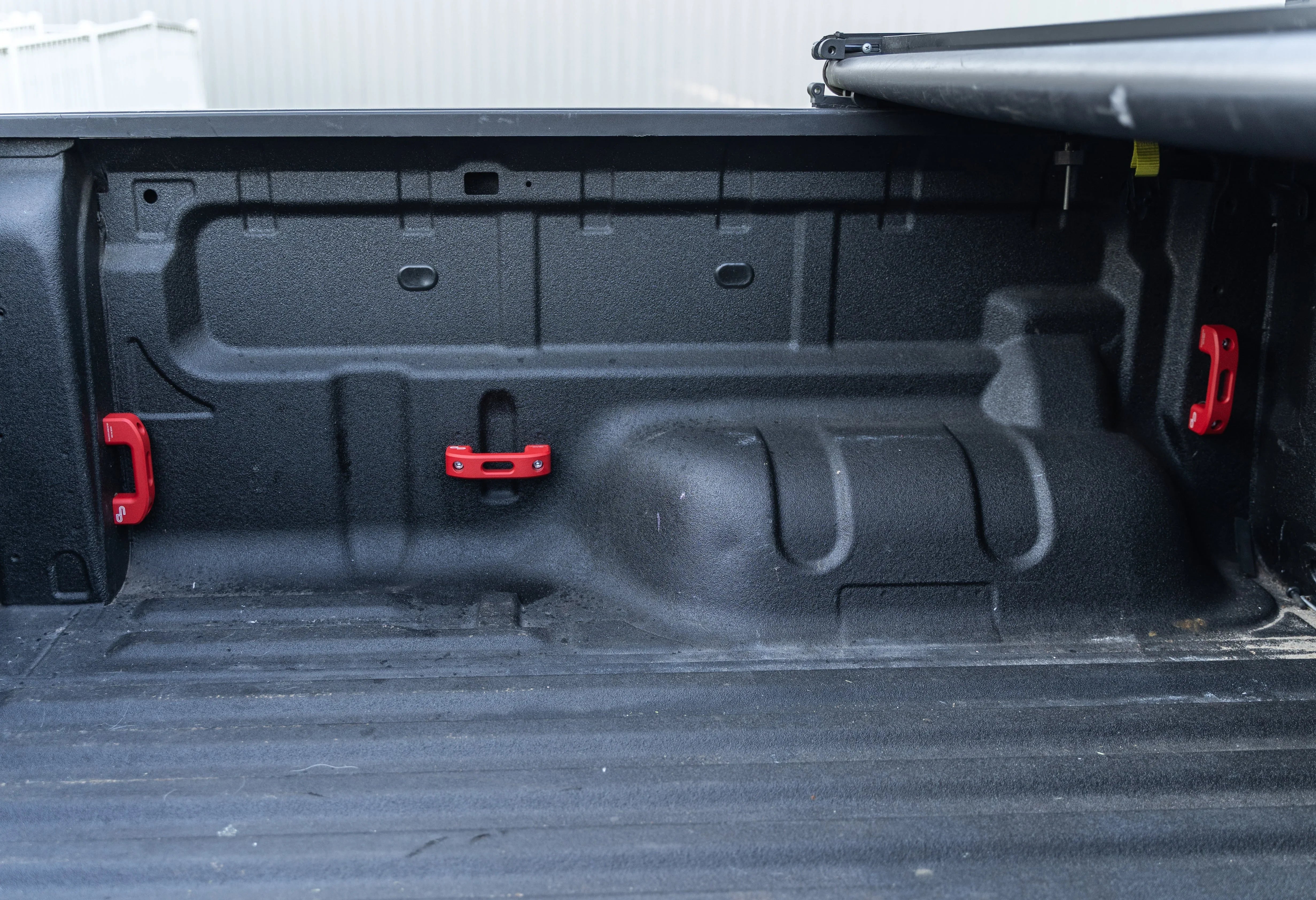 Truck bed interior with red tie-down anchors, textured liner, and roll-up tonneau cover