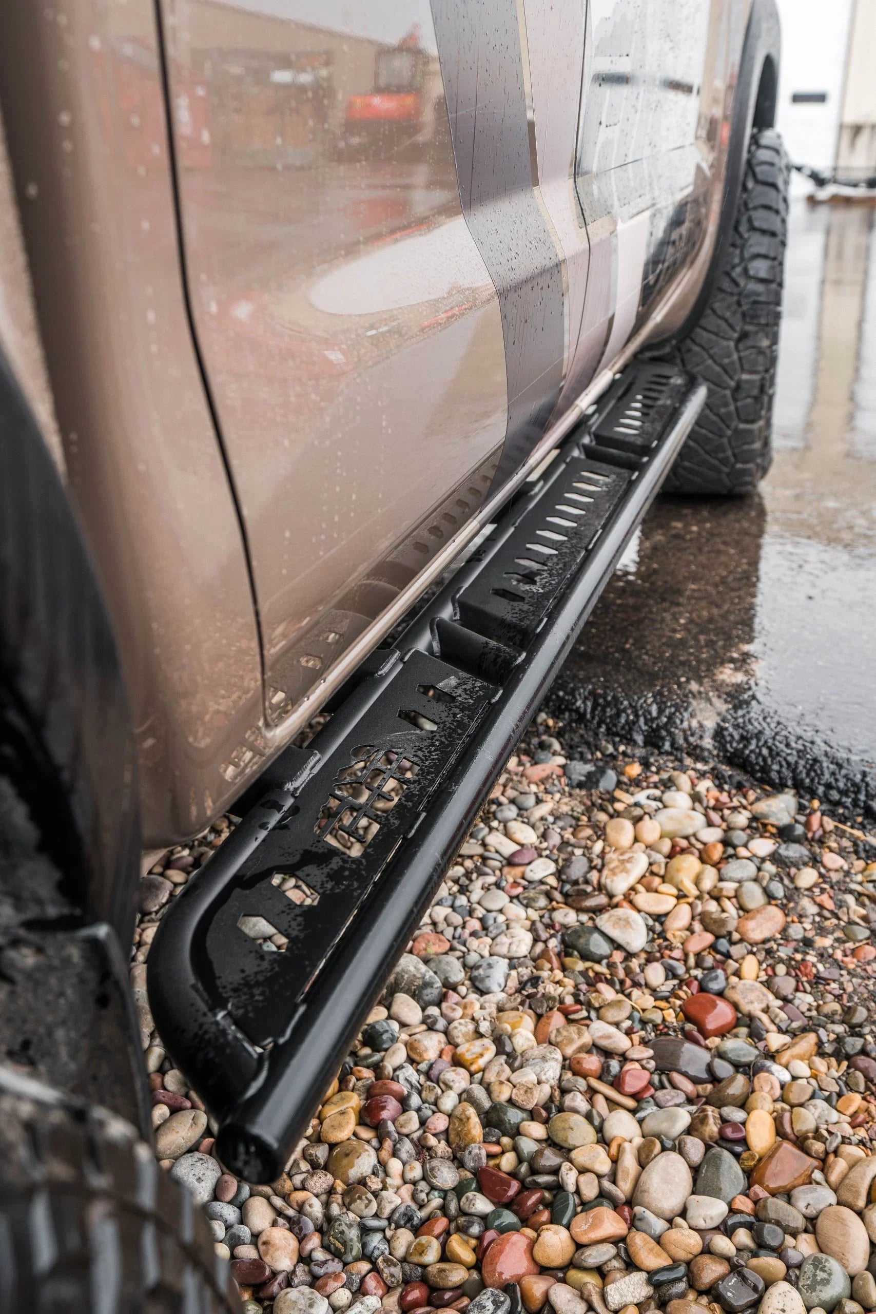 Close-up of black rock slider mounted on truck for off-road protection, wet surface detail