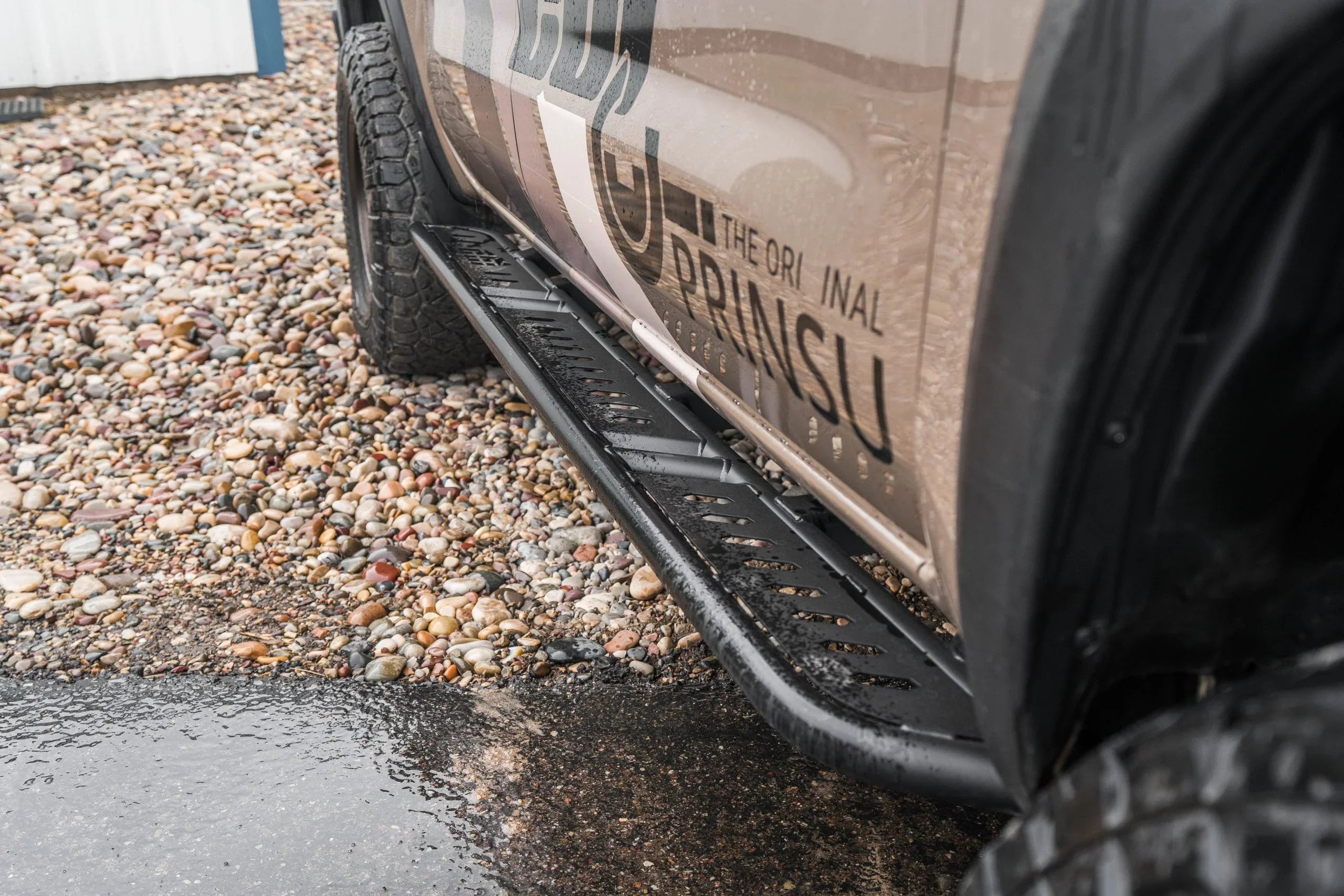 Black steel rock slider installed on off-road vehicle, parked on gravel