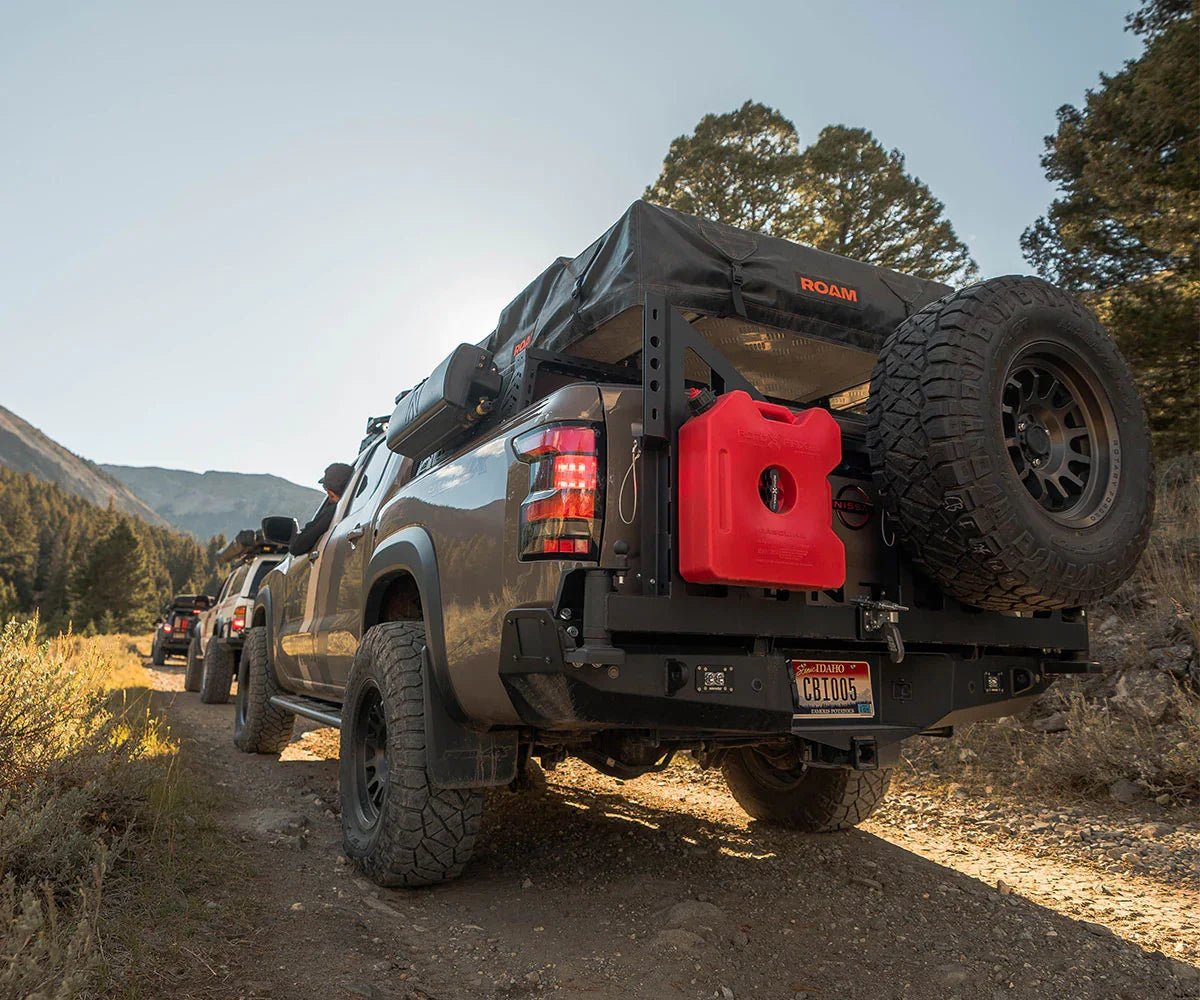 Off-road truck with roof tent, spare tire, and gear driving on a rugged forest trail