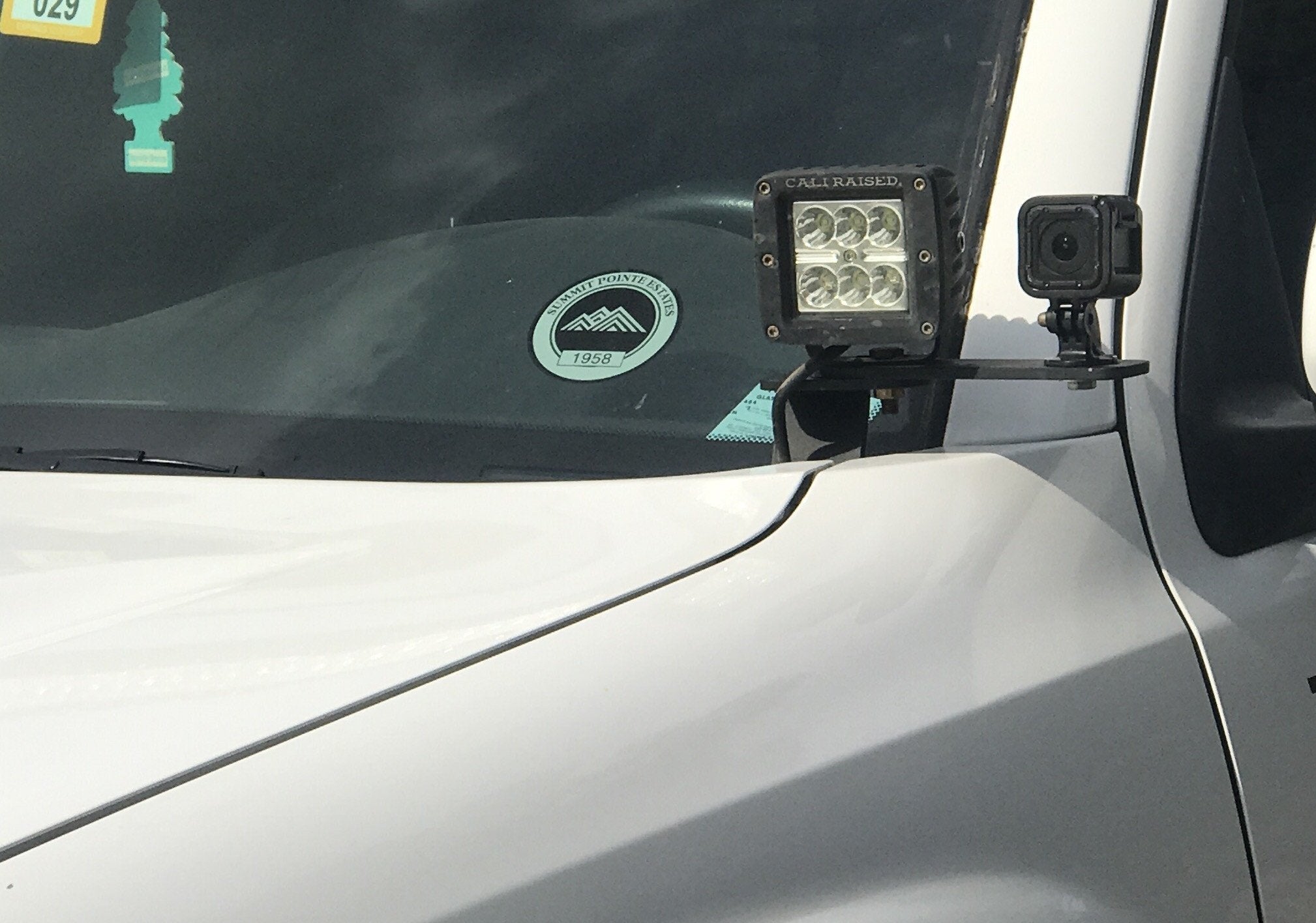 LED off-road pod light and action camera mounted on white truck hood for overlanding
