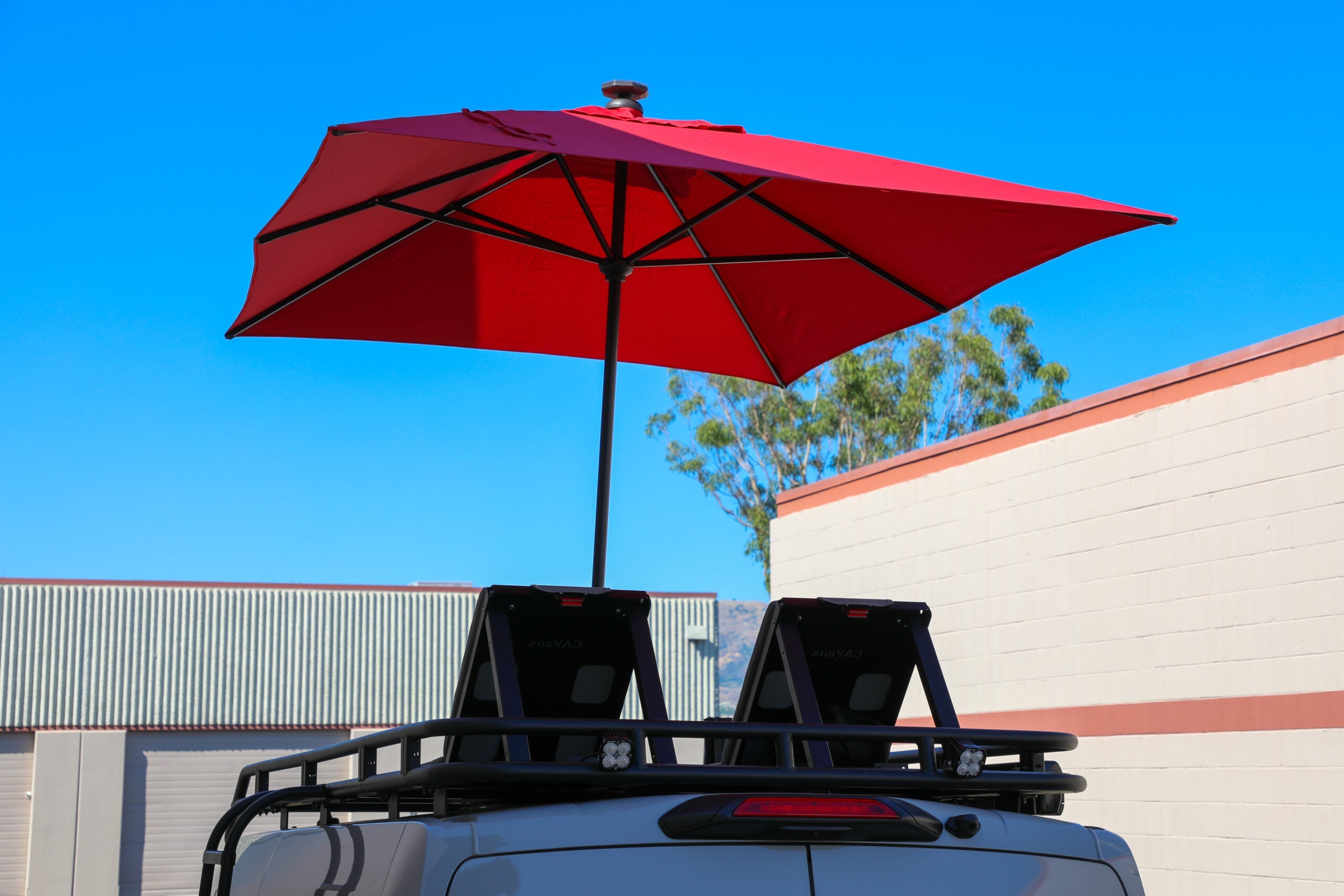 Red overland rooftop umbrella mounted on vehicle cargo rack under clear blue sky