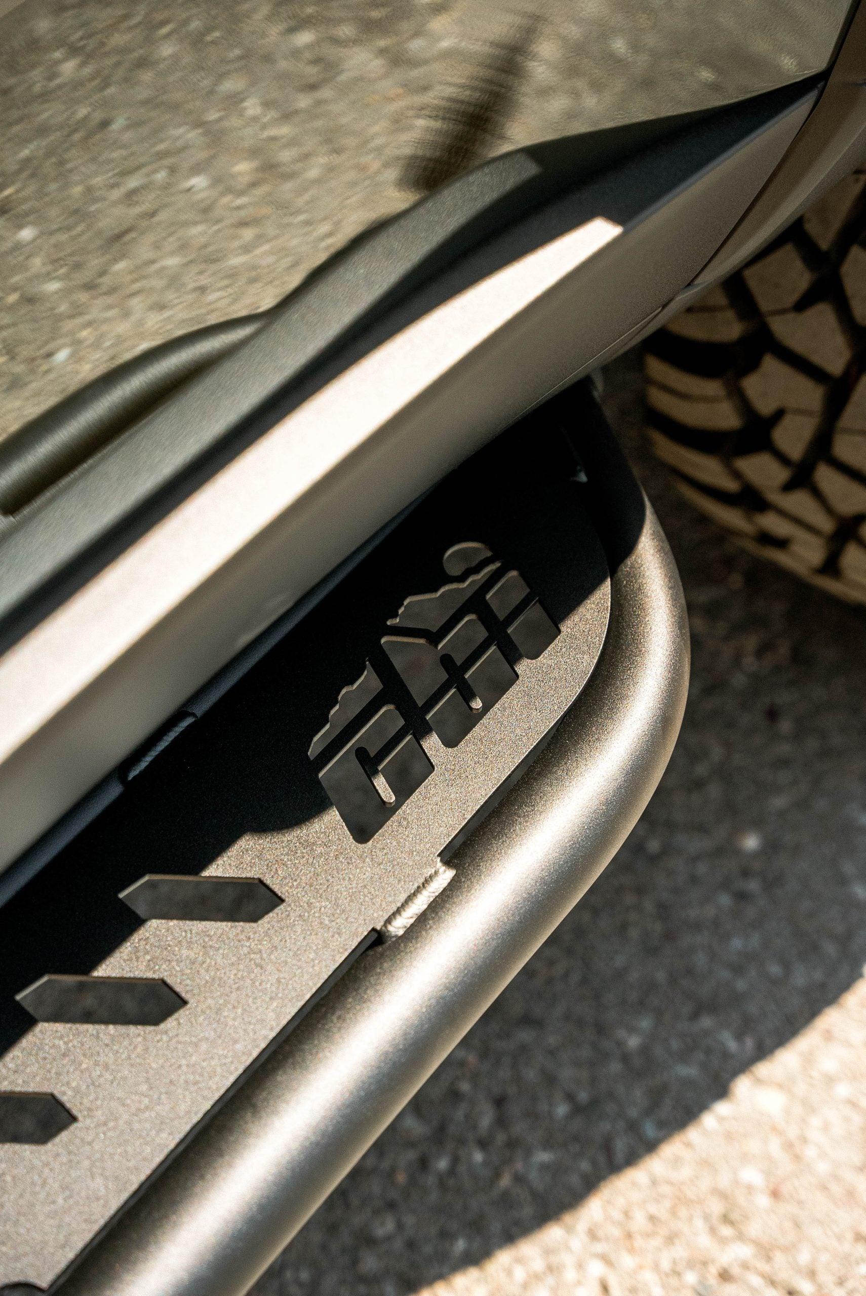 Close-up of off-road vehicle rock slider with mountain cutout design on metal step.