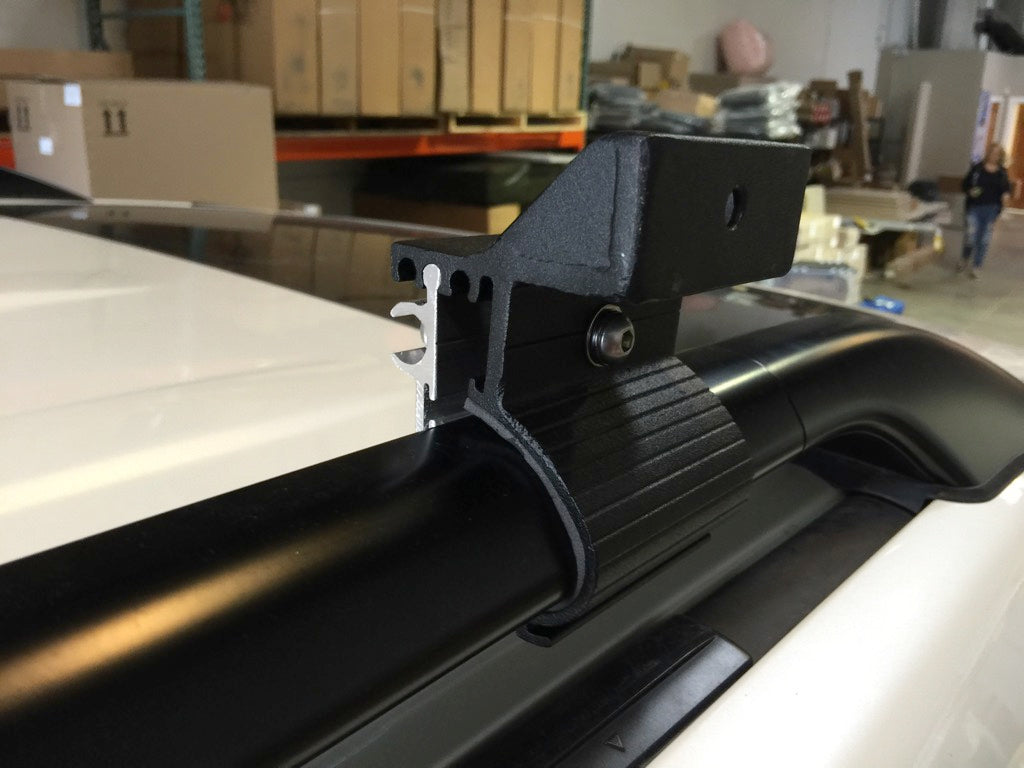 G clamp securely mounted on a black vehicle roof rack rail for overlanding accessories