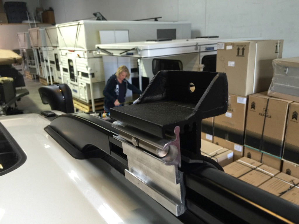 Heavy-duty G clamp mounted on vehicle roof rack in an overlanding gear warehouse