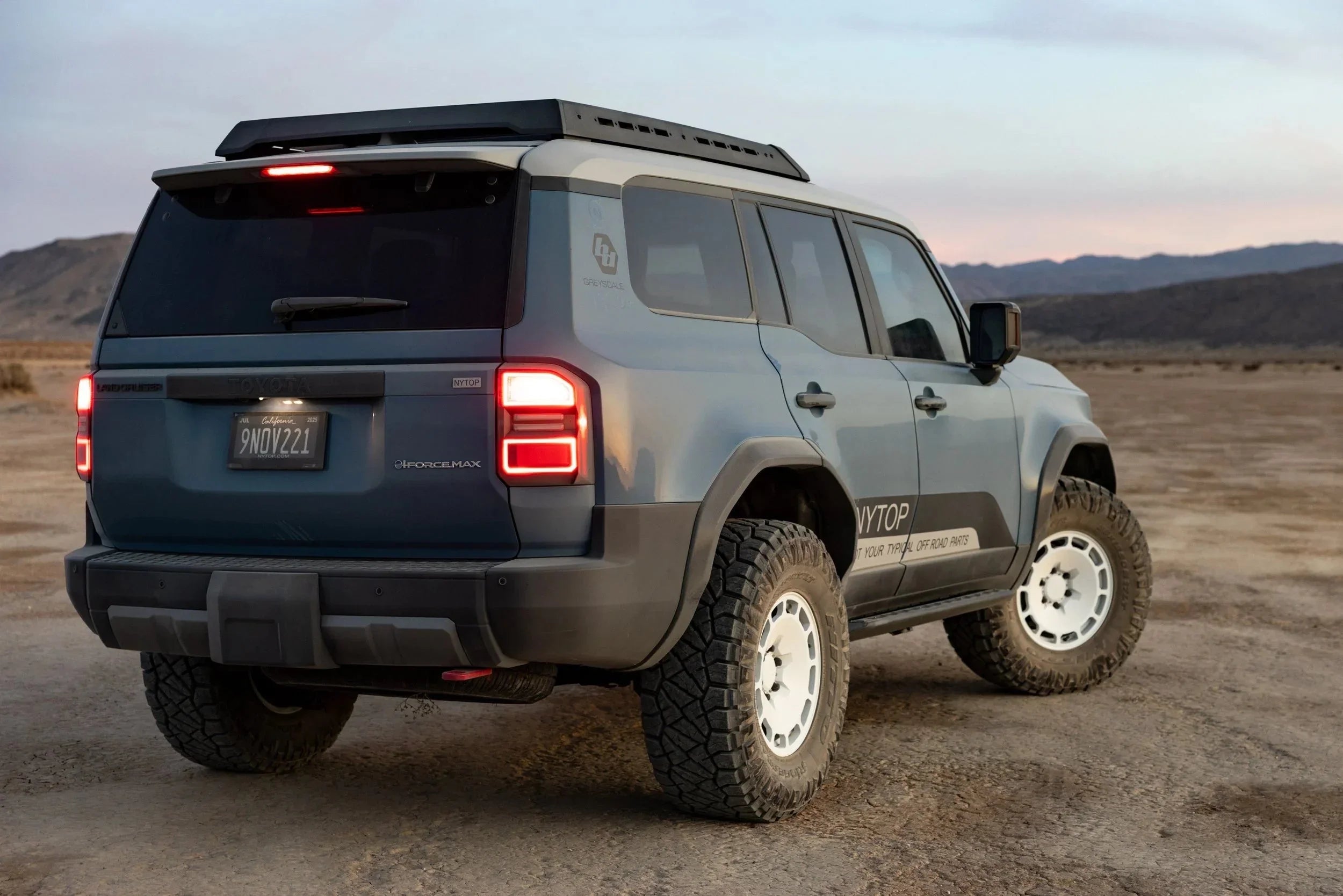 Toyota Land Cruiser SUV with off-road tires and roof rack parked on desert terrain at sunset