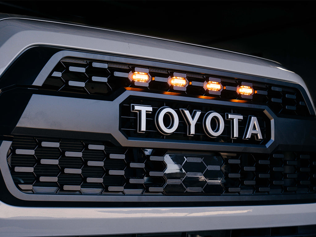 Toyota truck grille with bold lettering and amber LED marker lights, overland vehicle accessory
