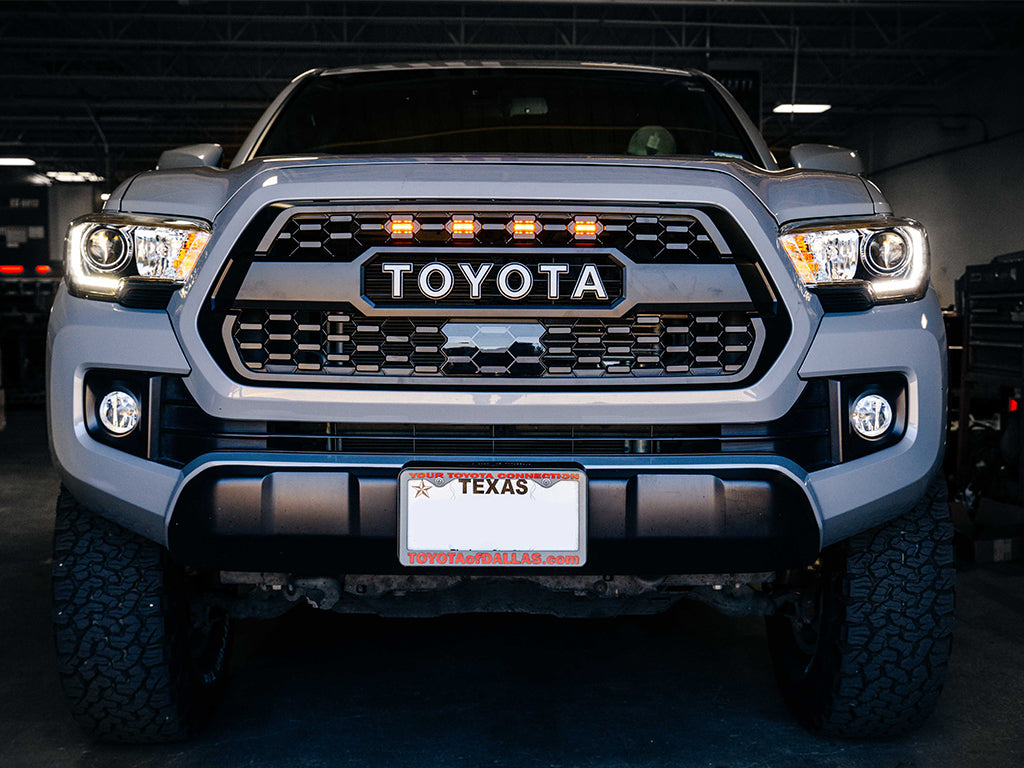 Front view of Toyota Tacoma with aftermarket grille and amber lights in a garage setting
