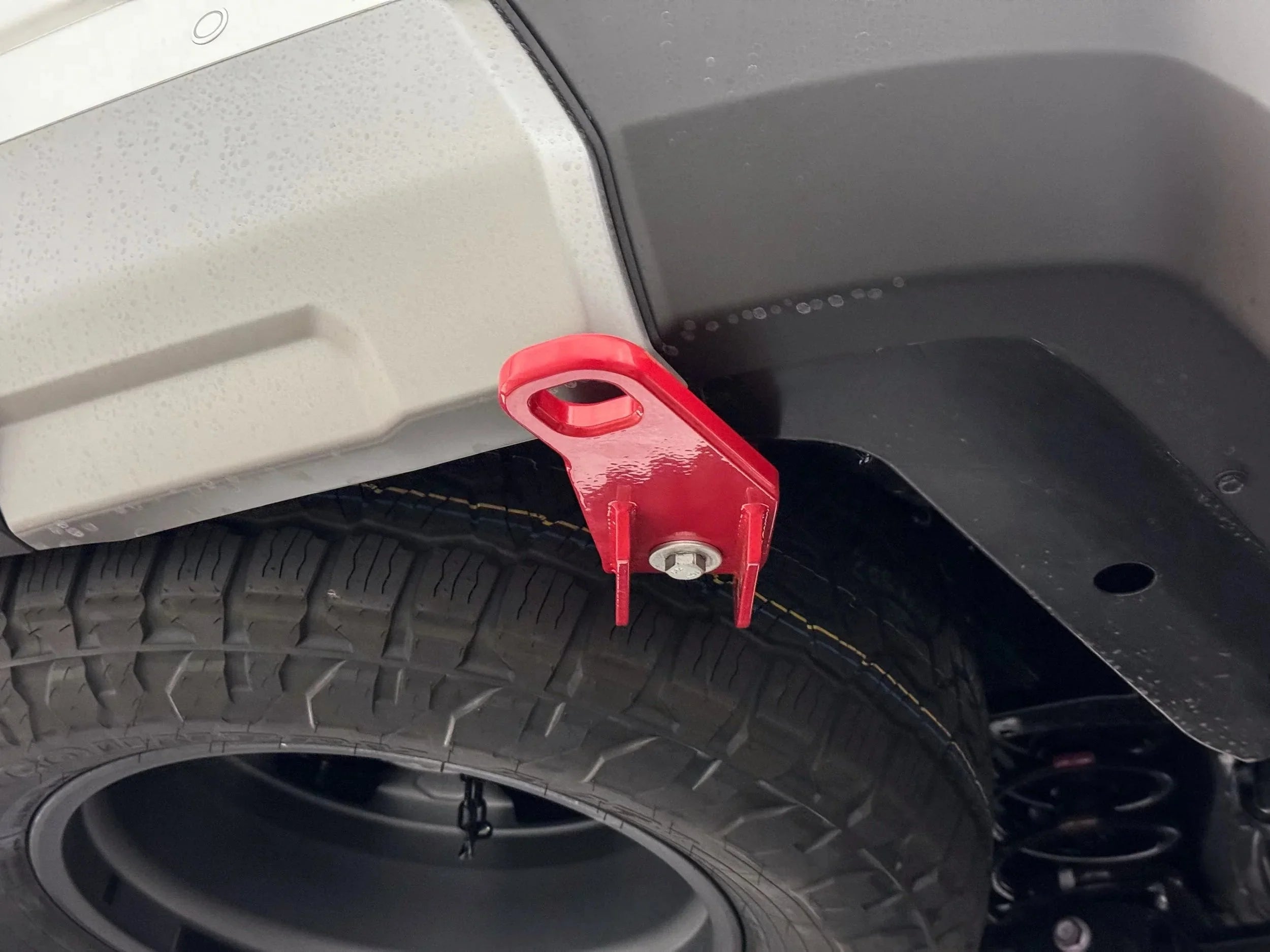 Red rear tow hook mounted on off-road vehicle near tire and bumper