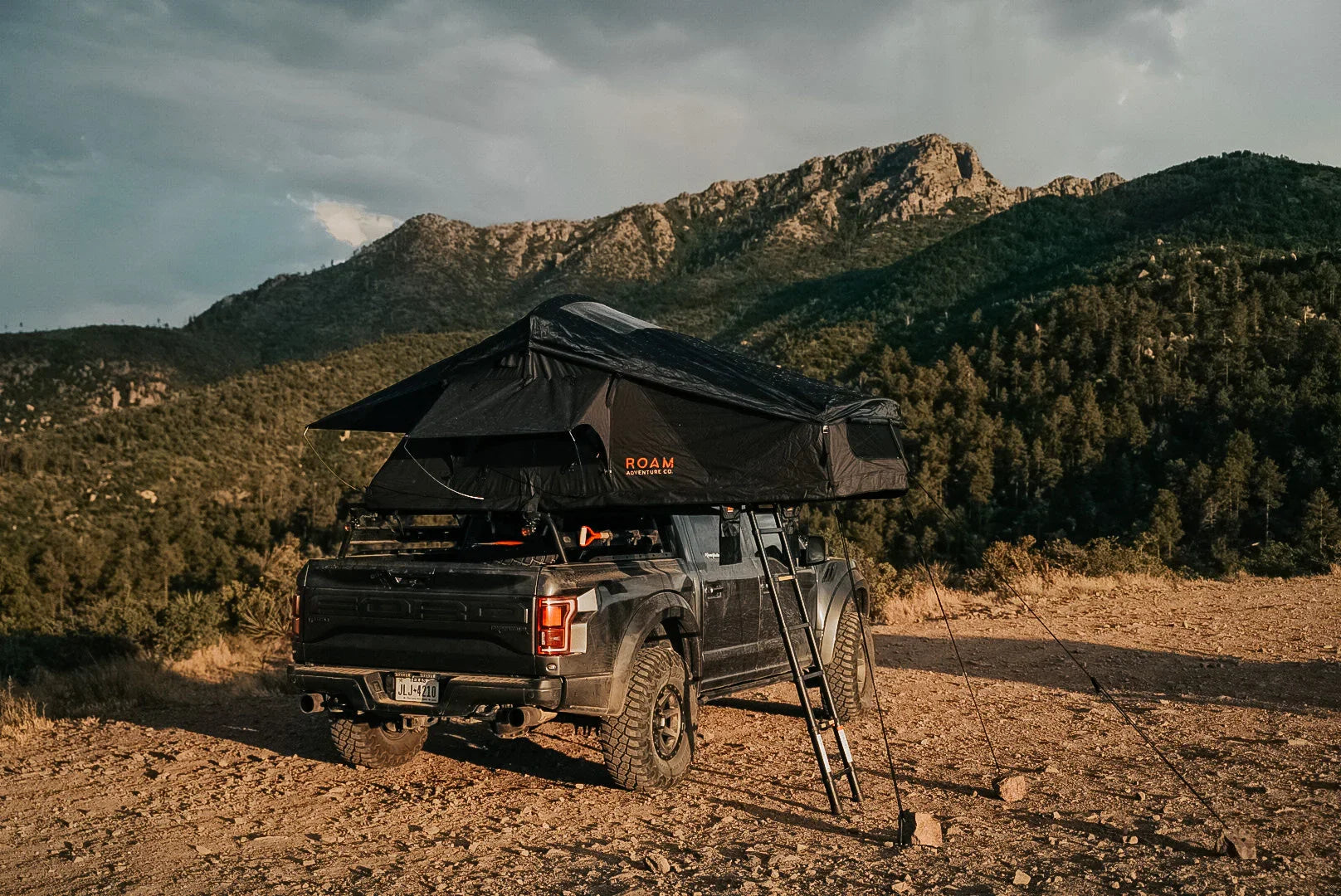 Off-road truck with rooftop tent setup for overlanding in a scenic mountain landscape.