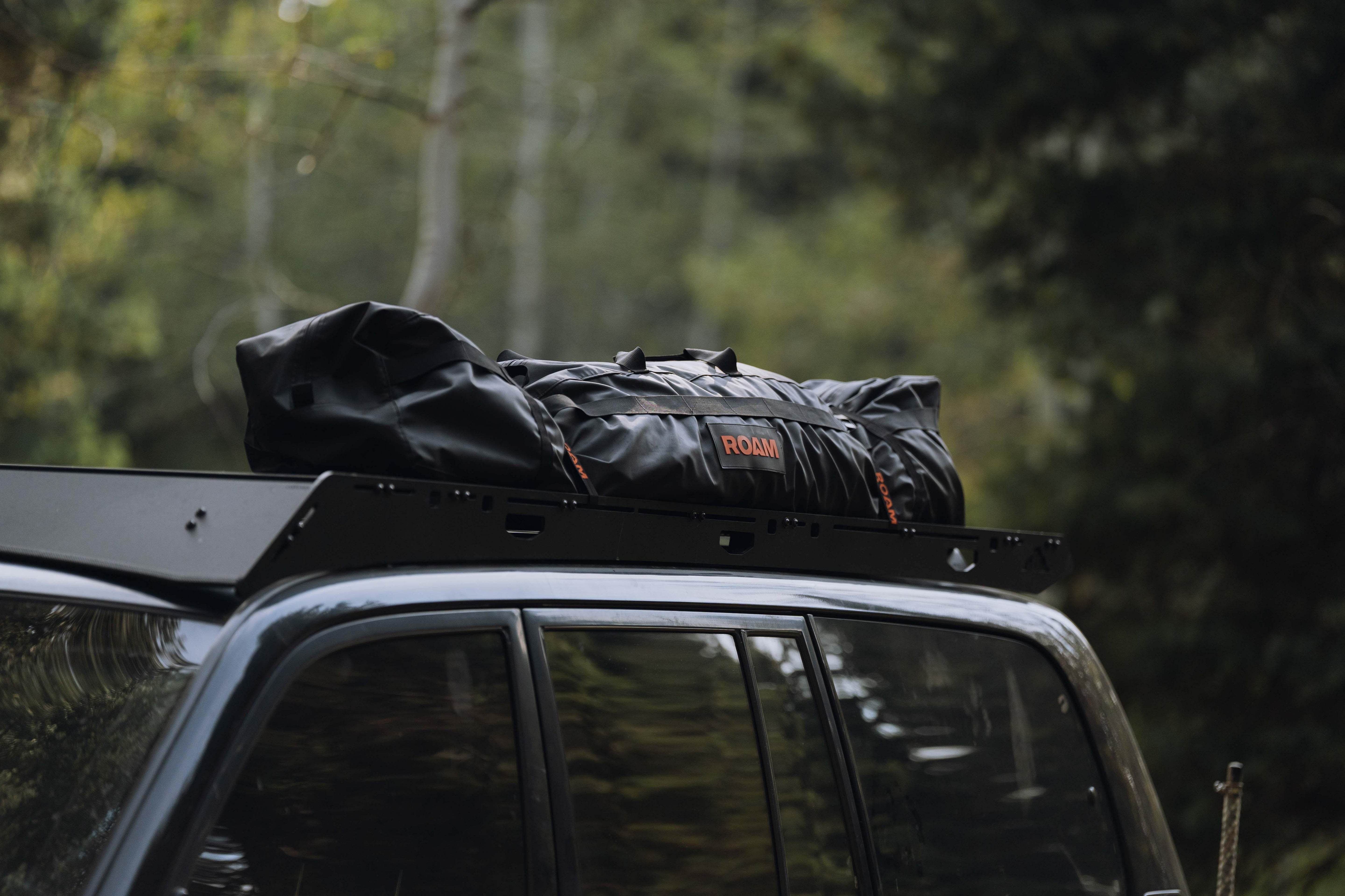 ROAM black rooftop cargo bag on SUV roof rack for overlanding in forest setting