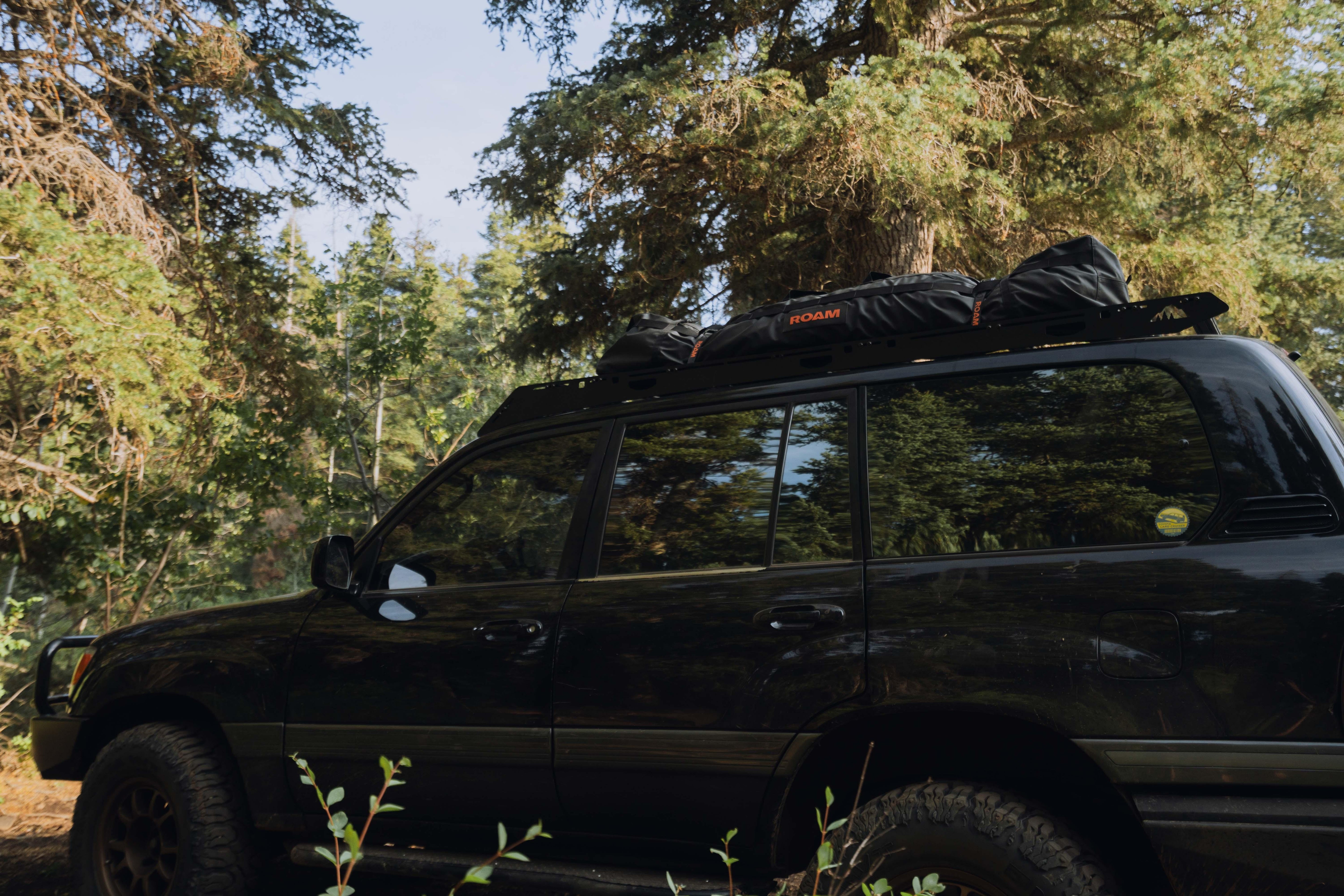 SUV with rooftop storage bag parked in forest, overlanding adventure gear visible