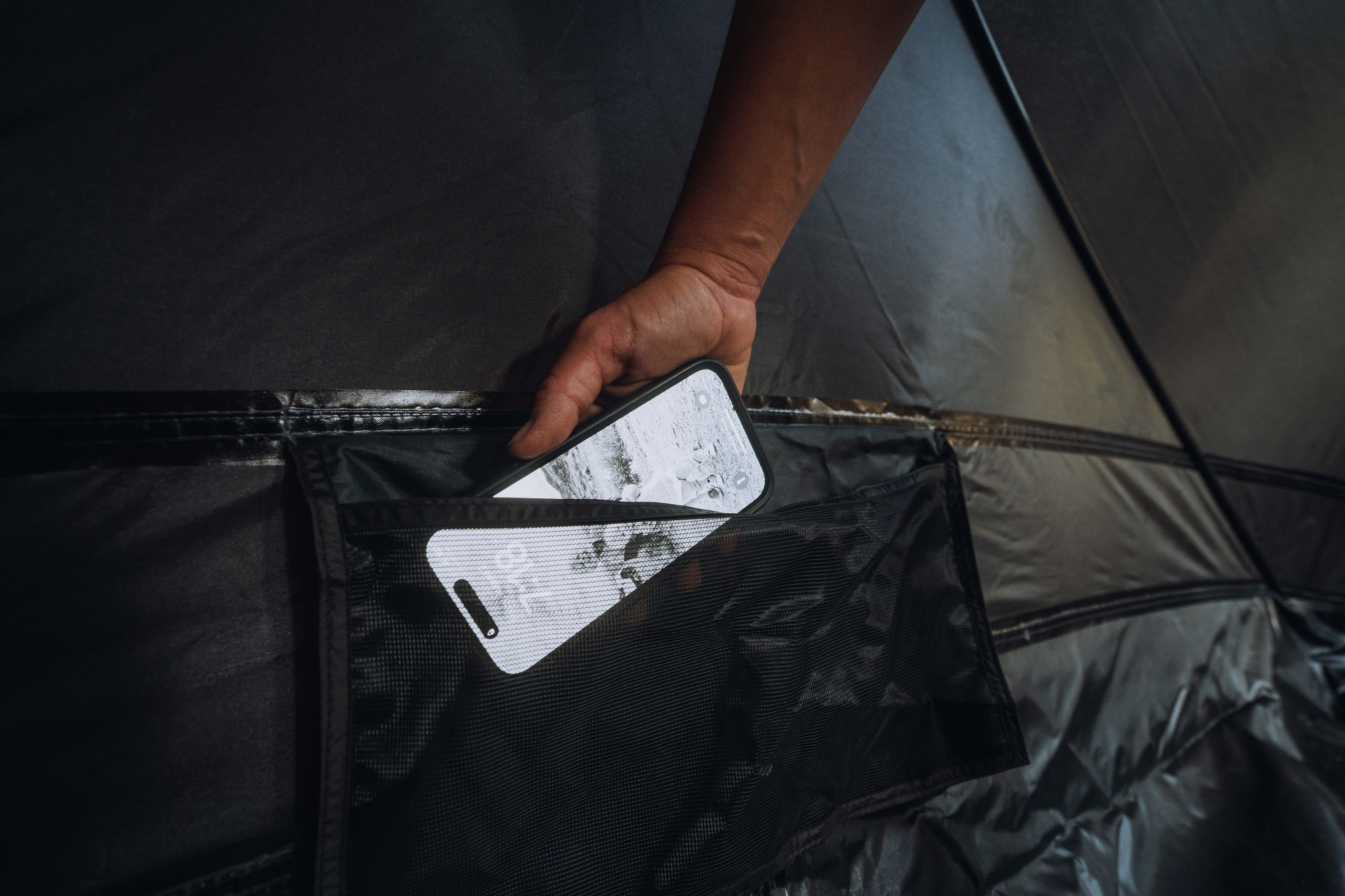 Hand placing a smartphone in a black mesh pocket inside a camping tent