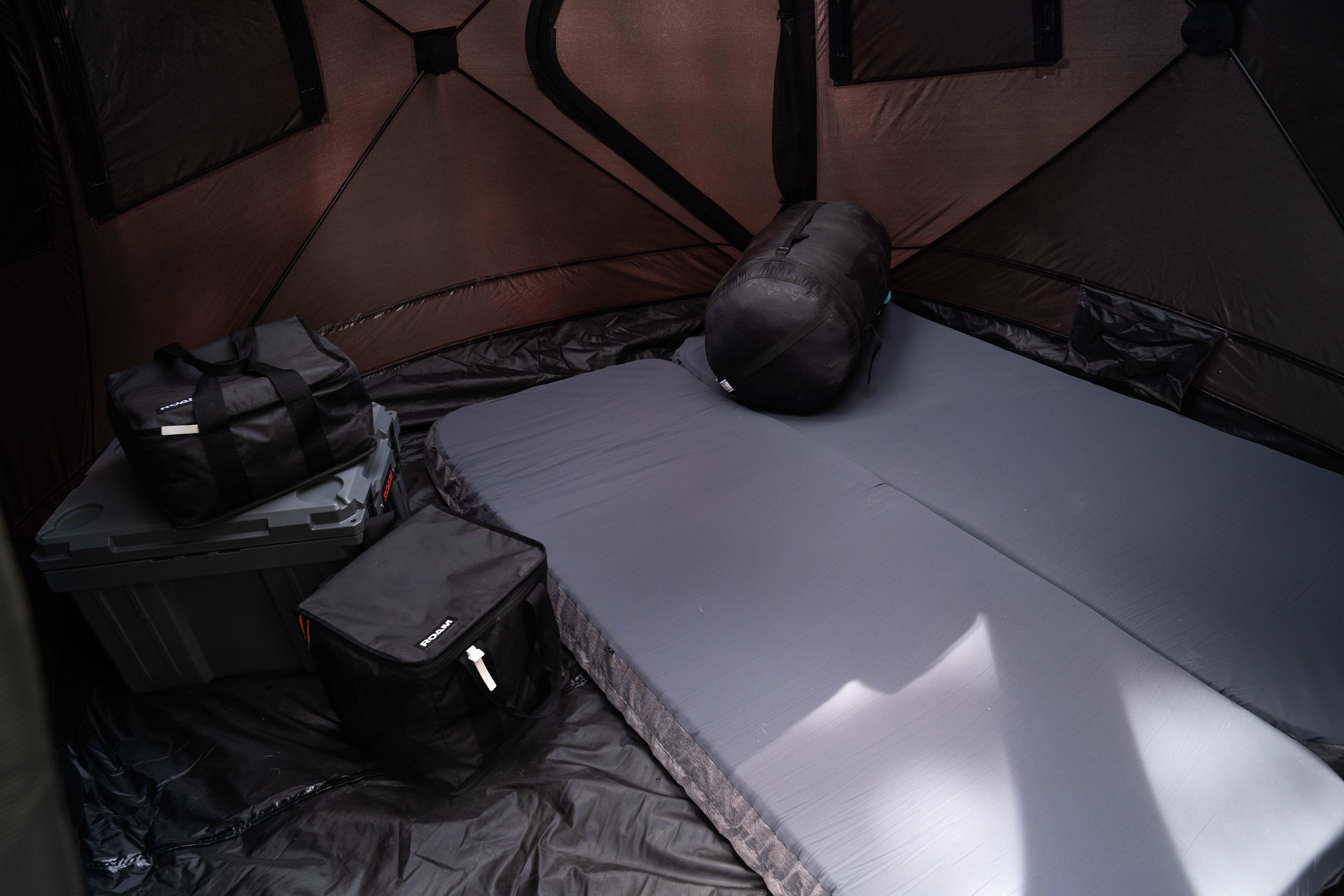 Interior of camping tent with foam mattress, storage bags, and gear container for overlanding