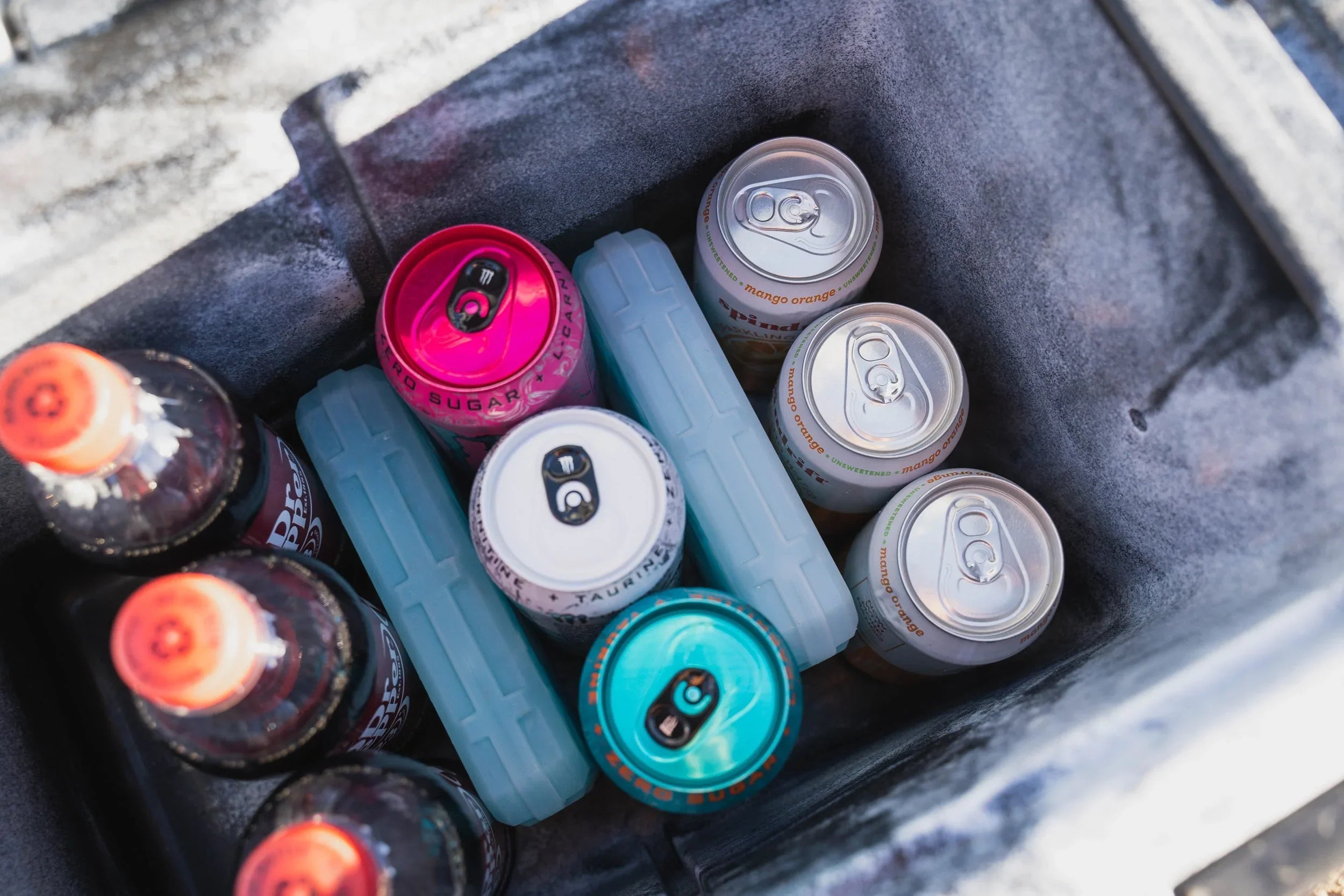 Assorted soda cans and bottles with ice packs inside a portable camping cooler