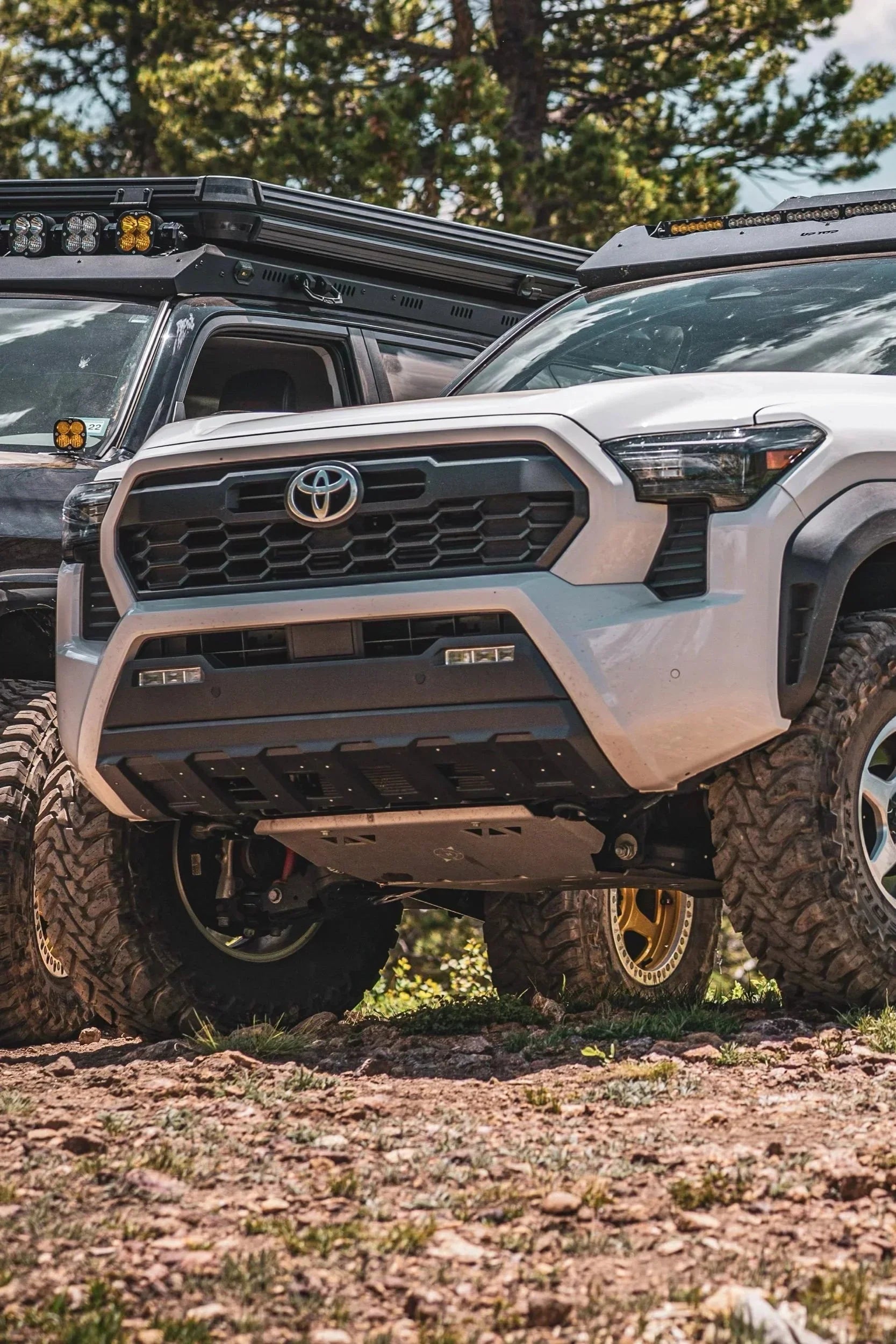 Lifted Toyota Tacoma trucks with off-road tires, aftermarket roof racks, and light bars on rocky terrain