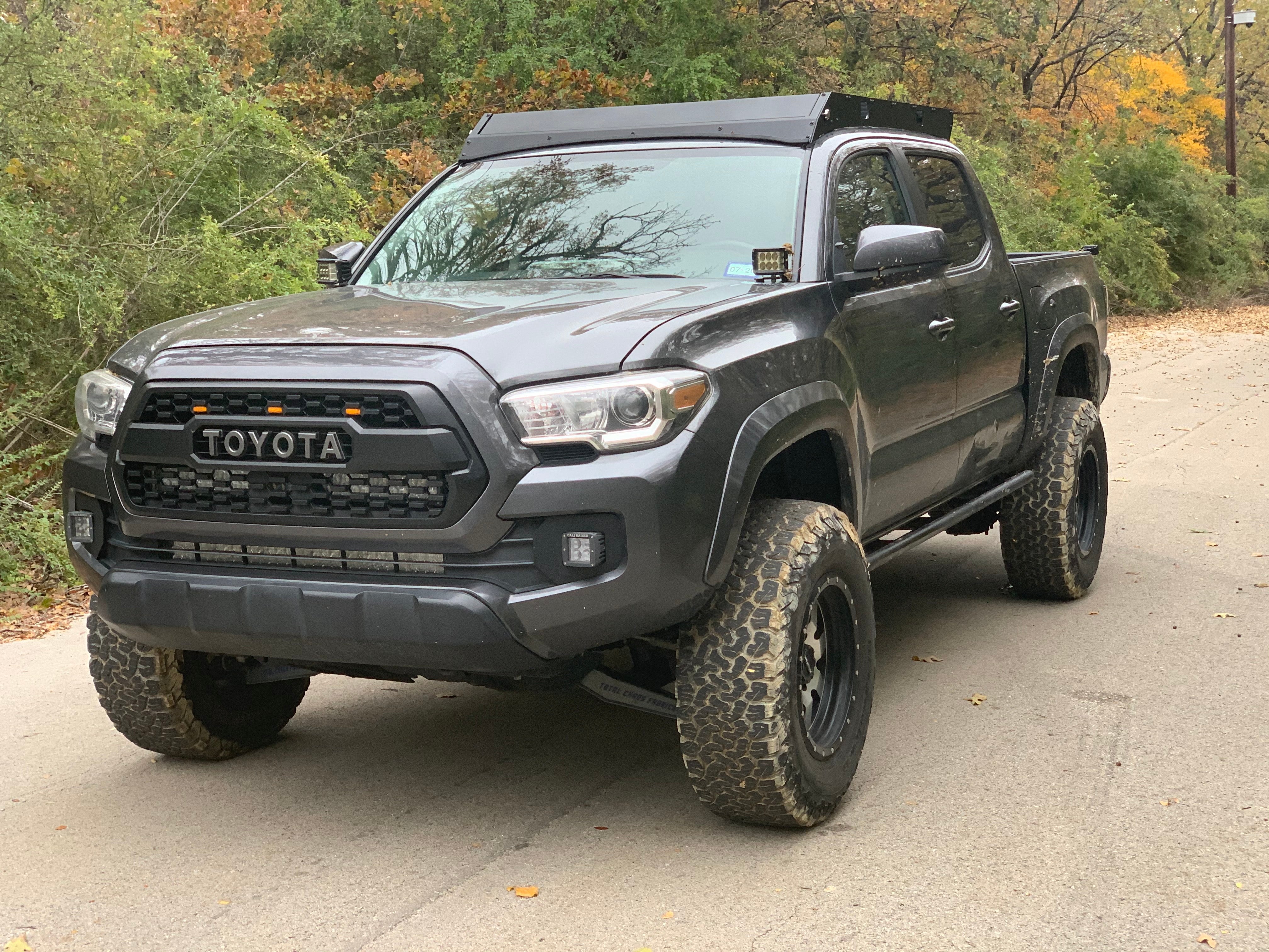 Lifted Toyota Tacoma with off-road tires and roof rack parked on a forest road