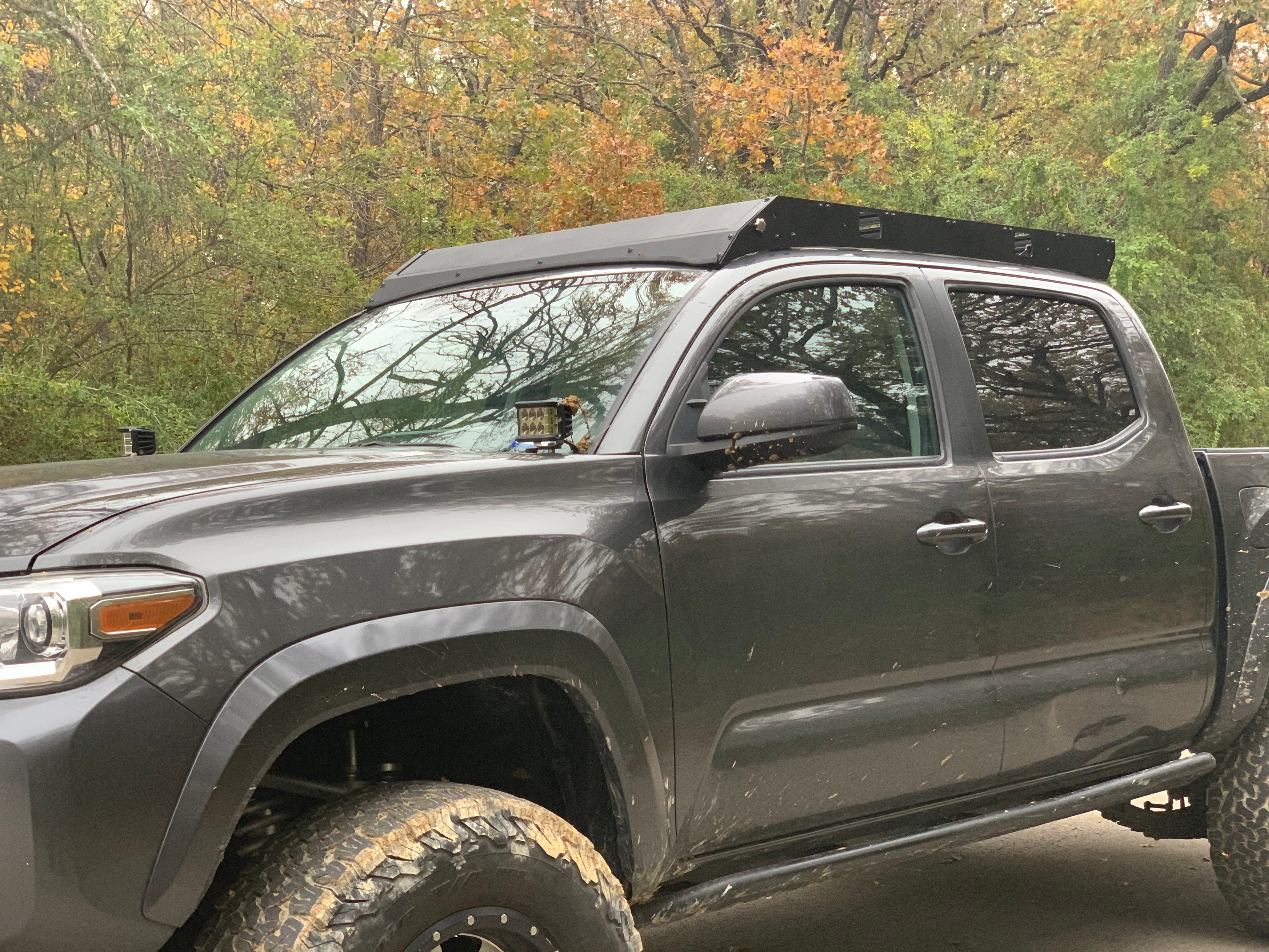 Toyota Tacoma with roof rack and off-road accessories in outdoor wooded setting