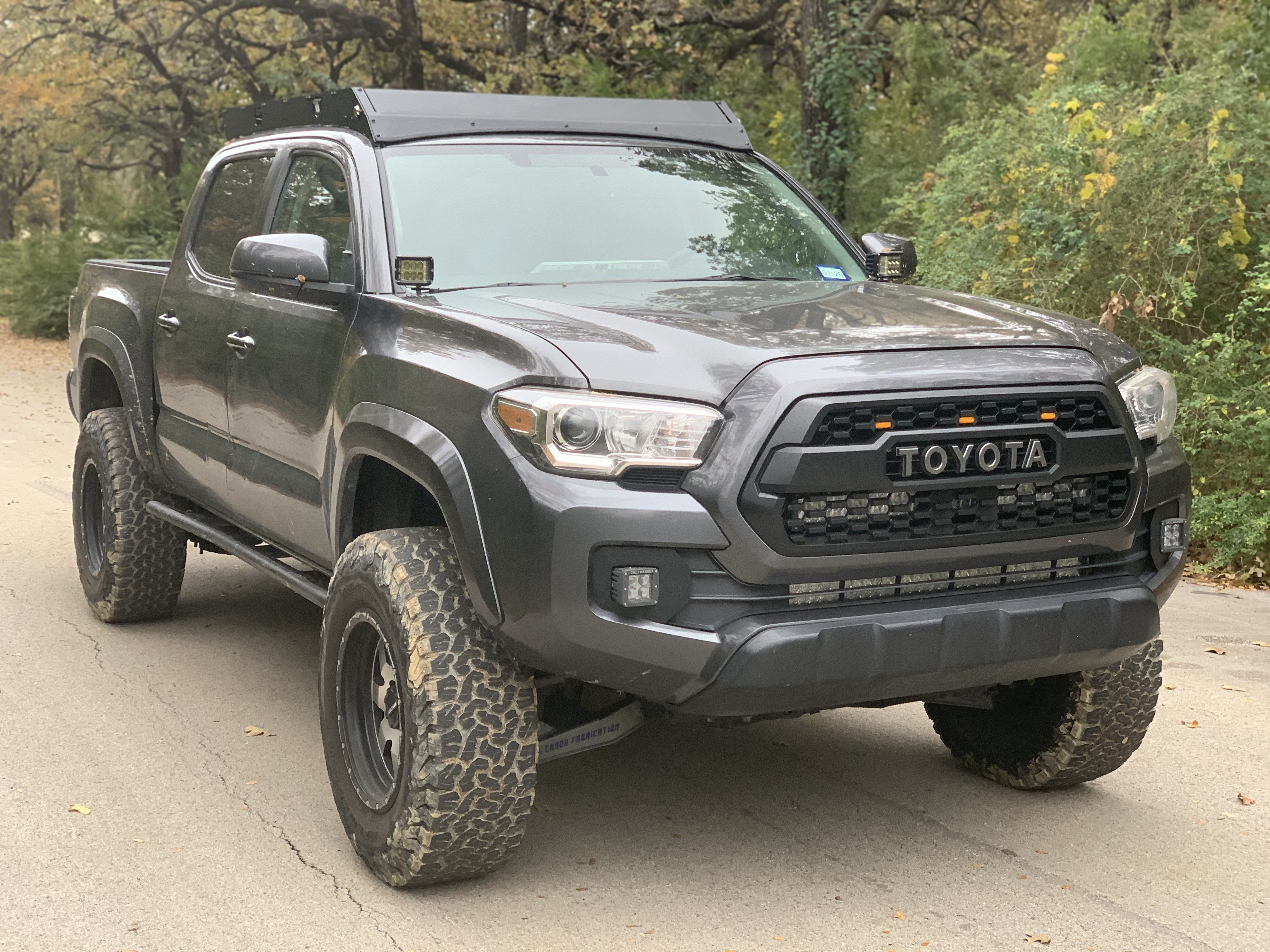 Lifted Toyota Tacoma with off-road tires and aftermarket roof rack on a forest road