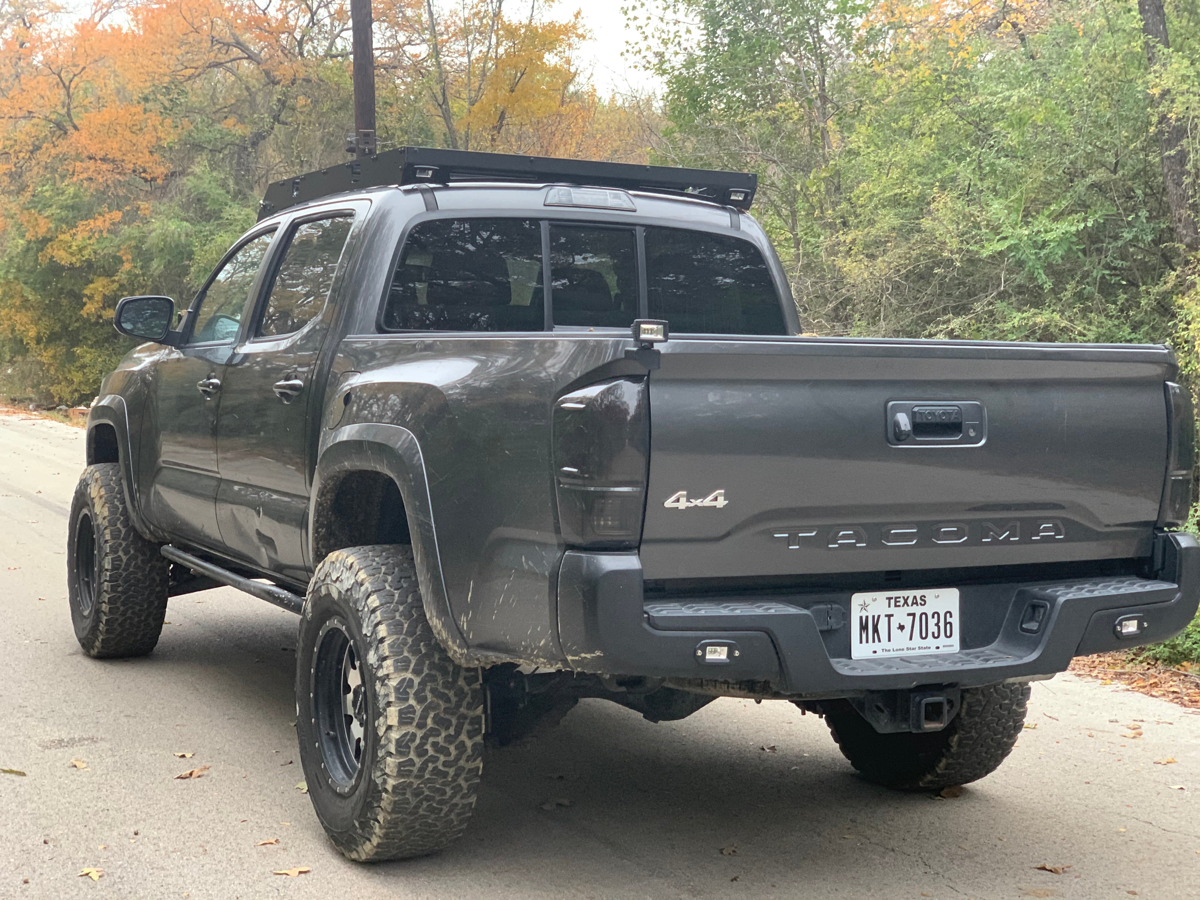 Lifted Toyota Tacoma 4x4 off-road truck with roof rack, mud tires, parked on forest road