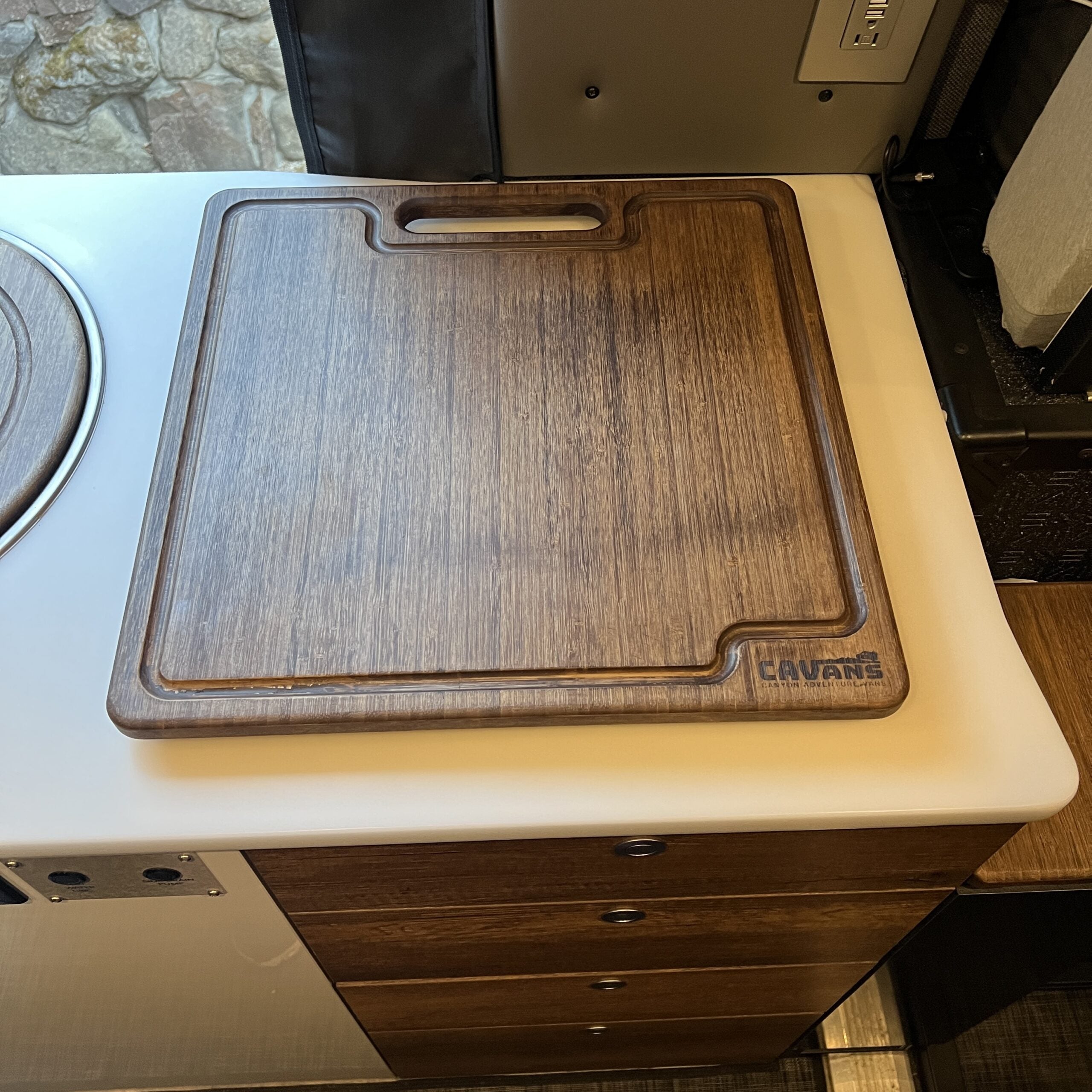 Wooden cutting board on camper kitchen counter with handle and juice groove, overland gear