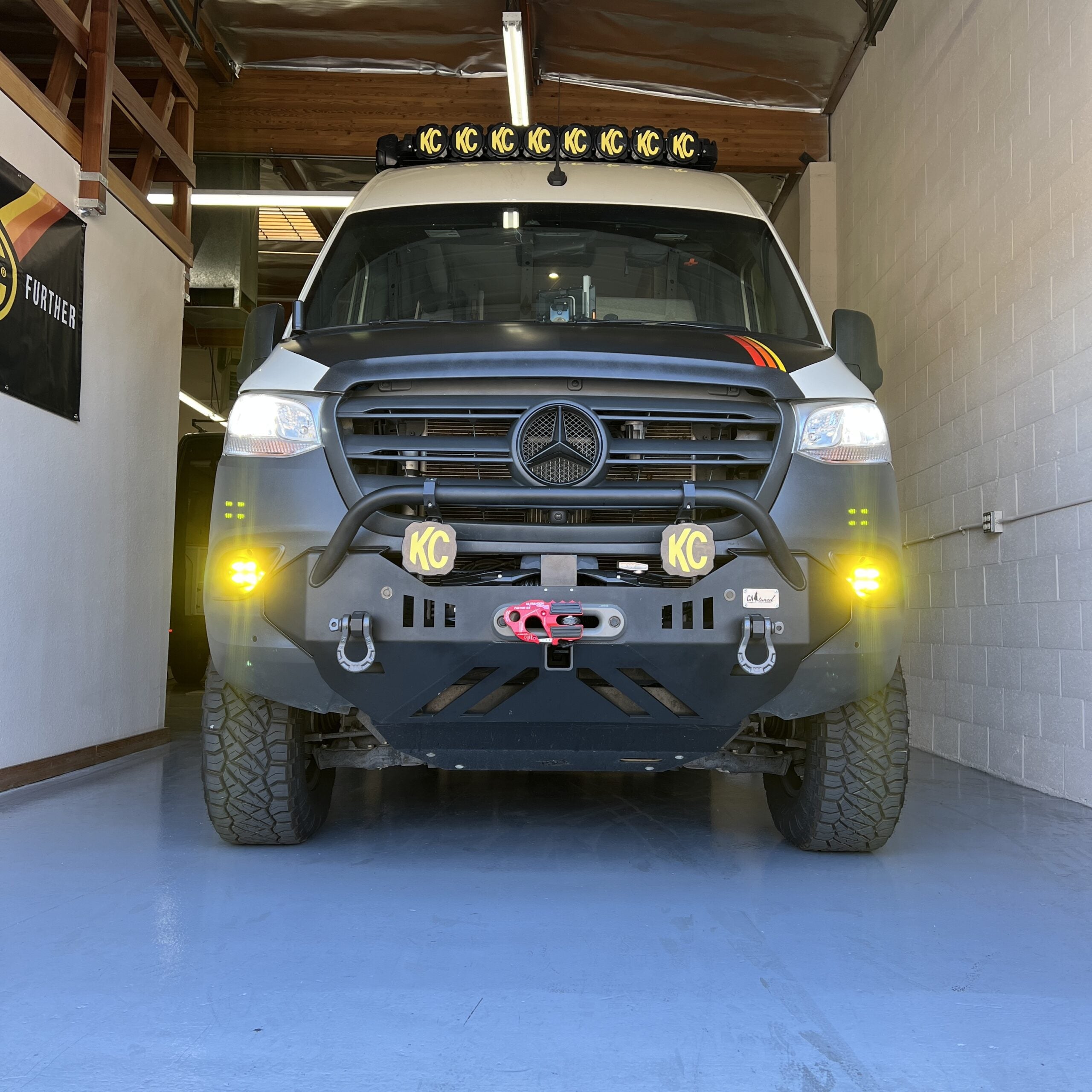 Mercedes Sprinter van with KC off-road lights and rugged front bumper in a garage