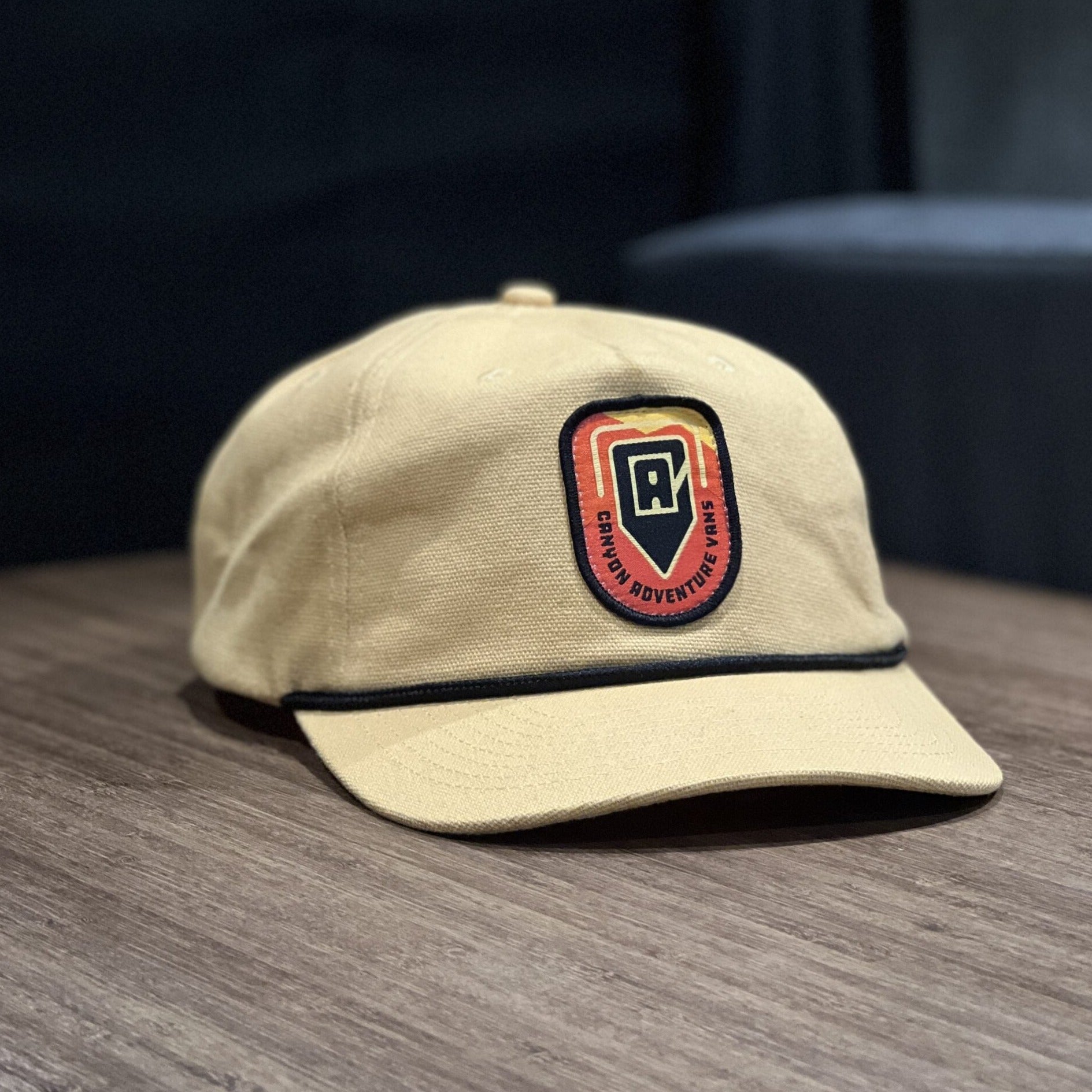 Beige adventure hat with Canyon Adventure Vans patch on wooden table, camping gear accessory