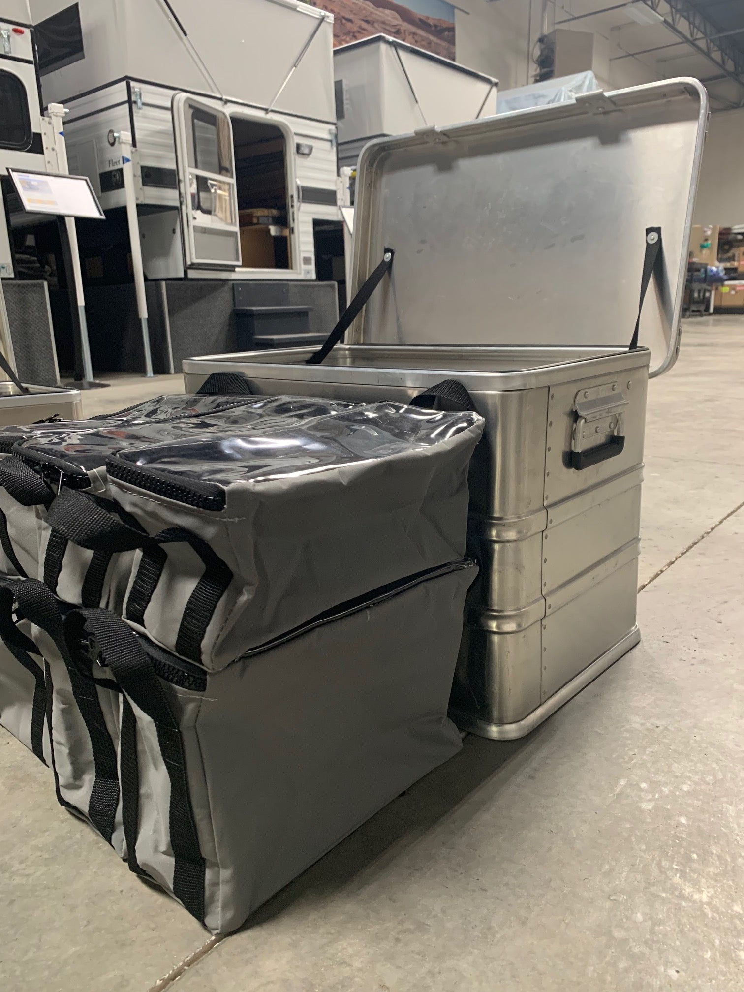 Heavy-duty aluminum storage box with open lid and gray soft bags for overlanding gear indoors
