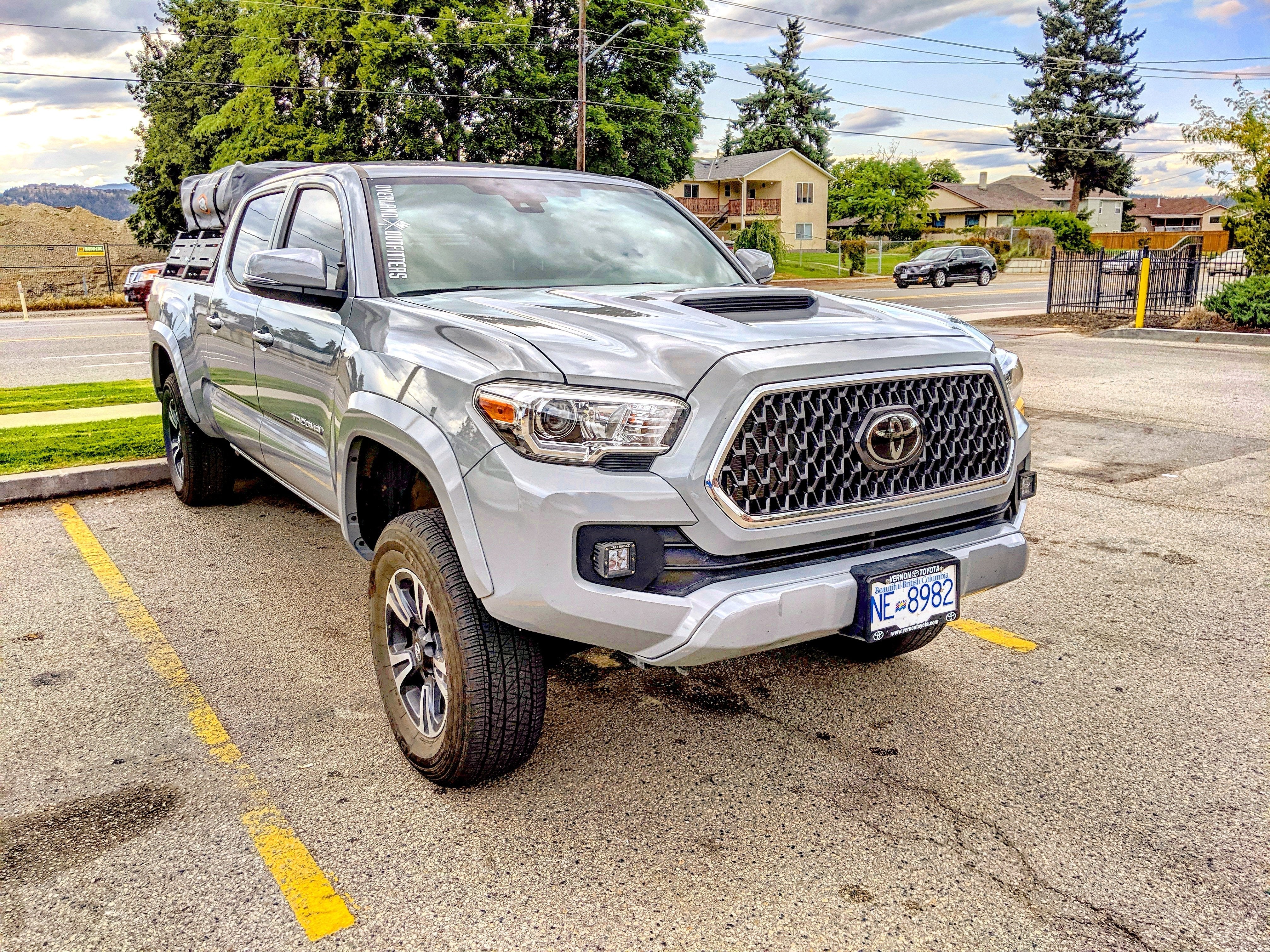 Silver Toyota Tacoma with off-road rack and gear, parked outdoors in a suburban setting.