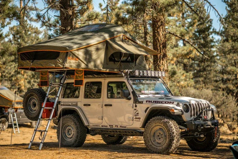Jeep Wrangler with rooftop tent and overlanding gear parked at forest campsite