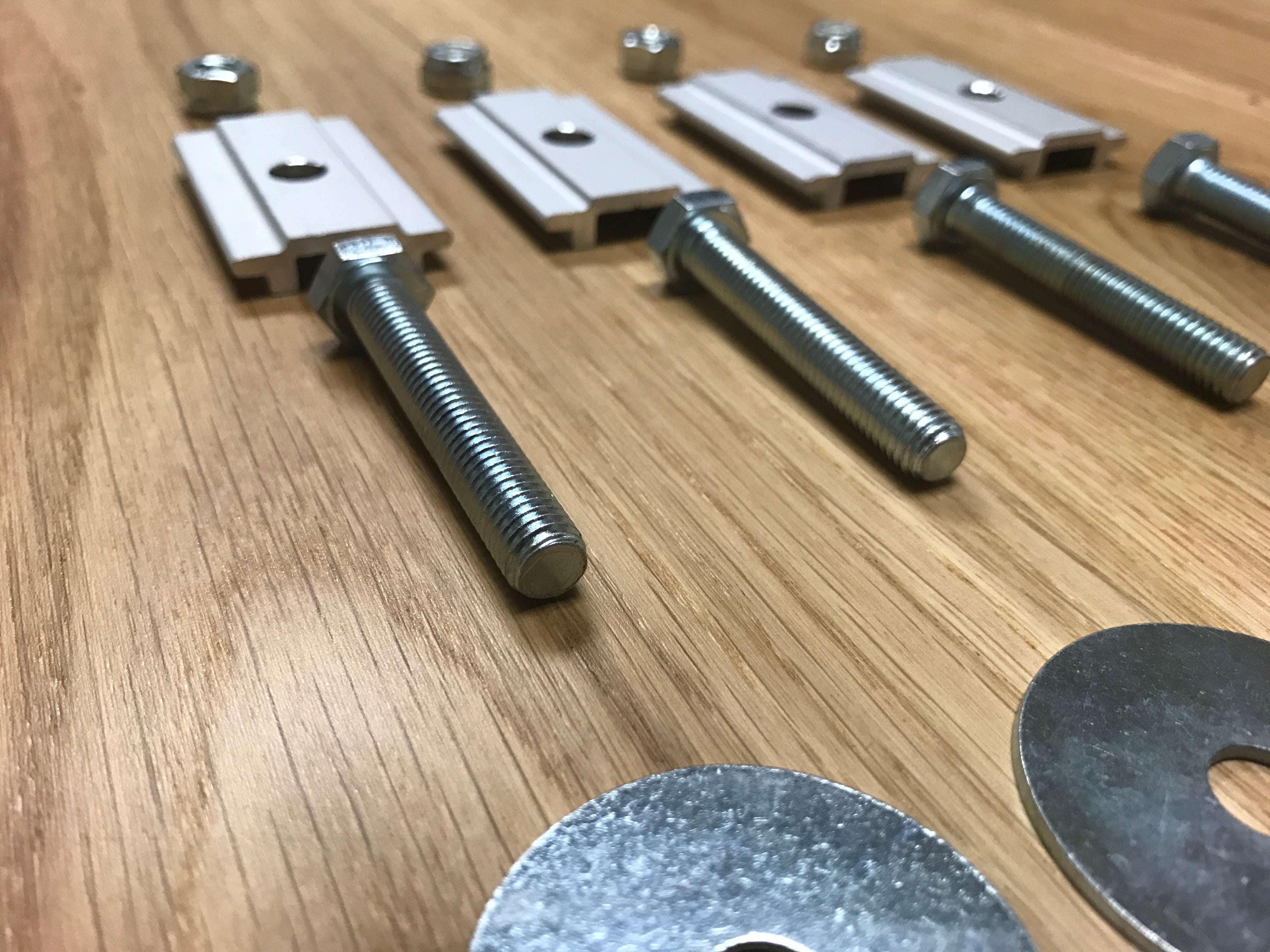 Close-up of metal bolts, washers, nuts, and mounting brackets on a wooden surface, hardware for vehicle accessories installation.