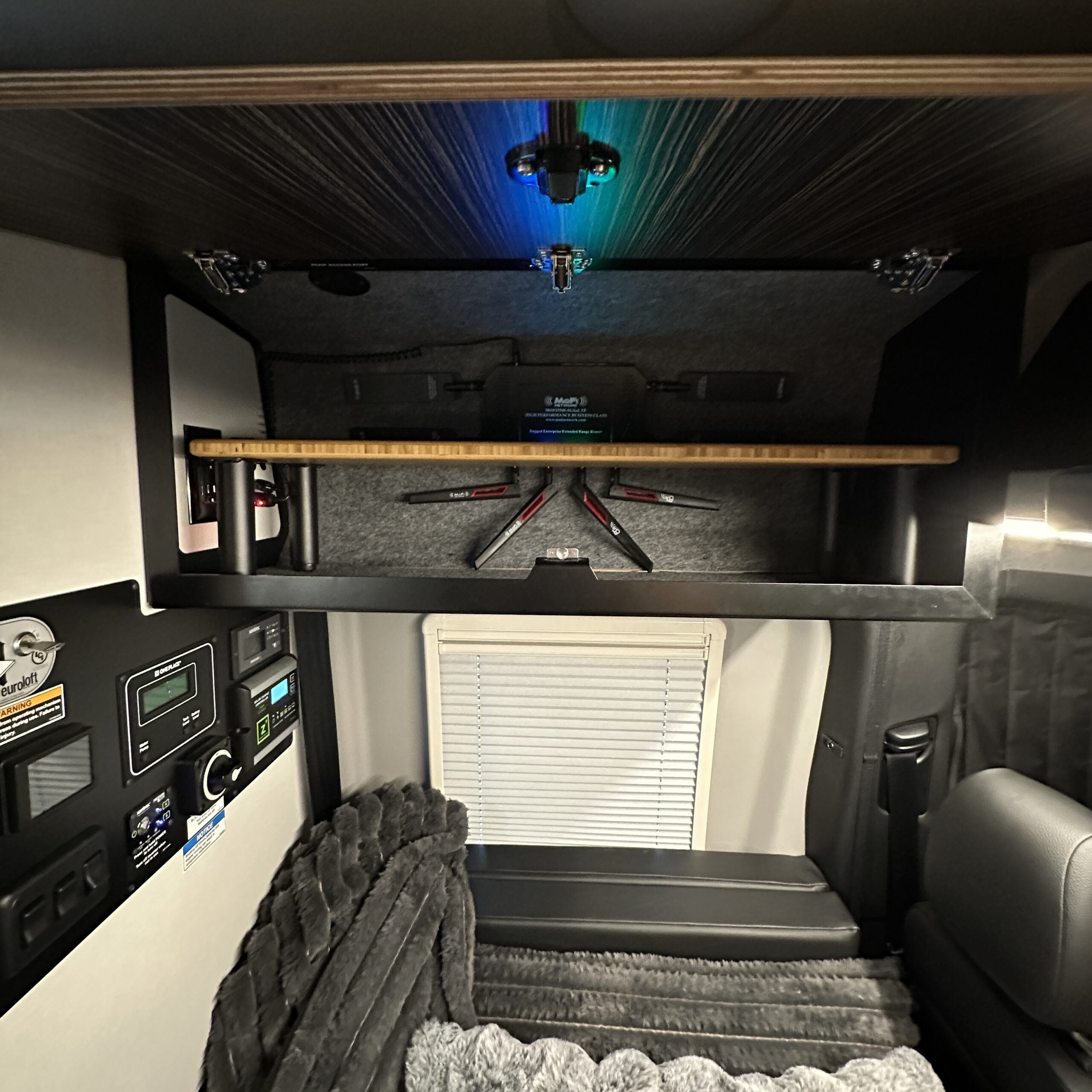 Overlanding camper interior with gear storage, control panel, and cozy bedding