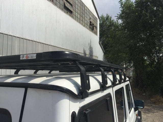 Heavy-duty roof rack on white off-road vehicle parked by industrial building, ideal for overlanding