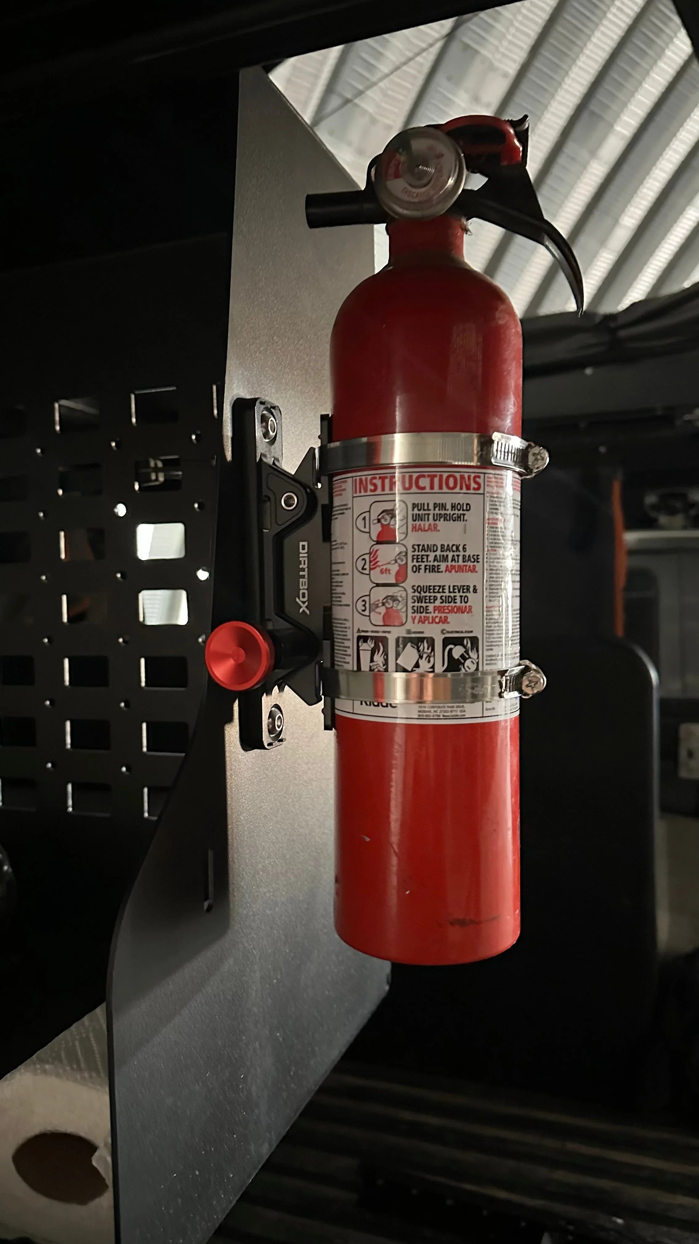 Red fire extinguisher mounted on an off-road vehicle interior accessory panel.