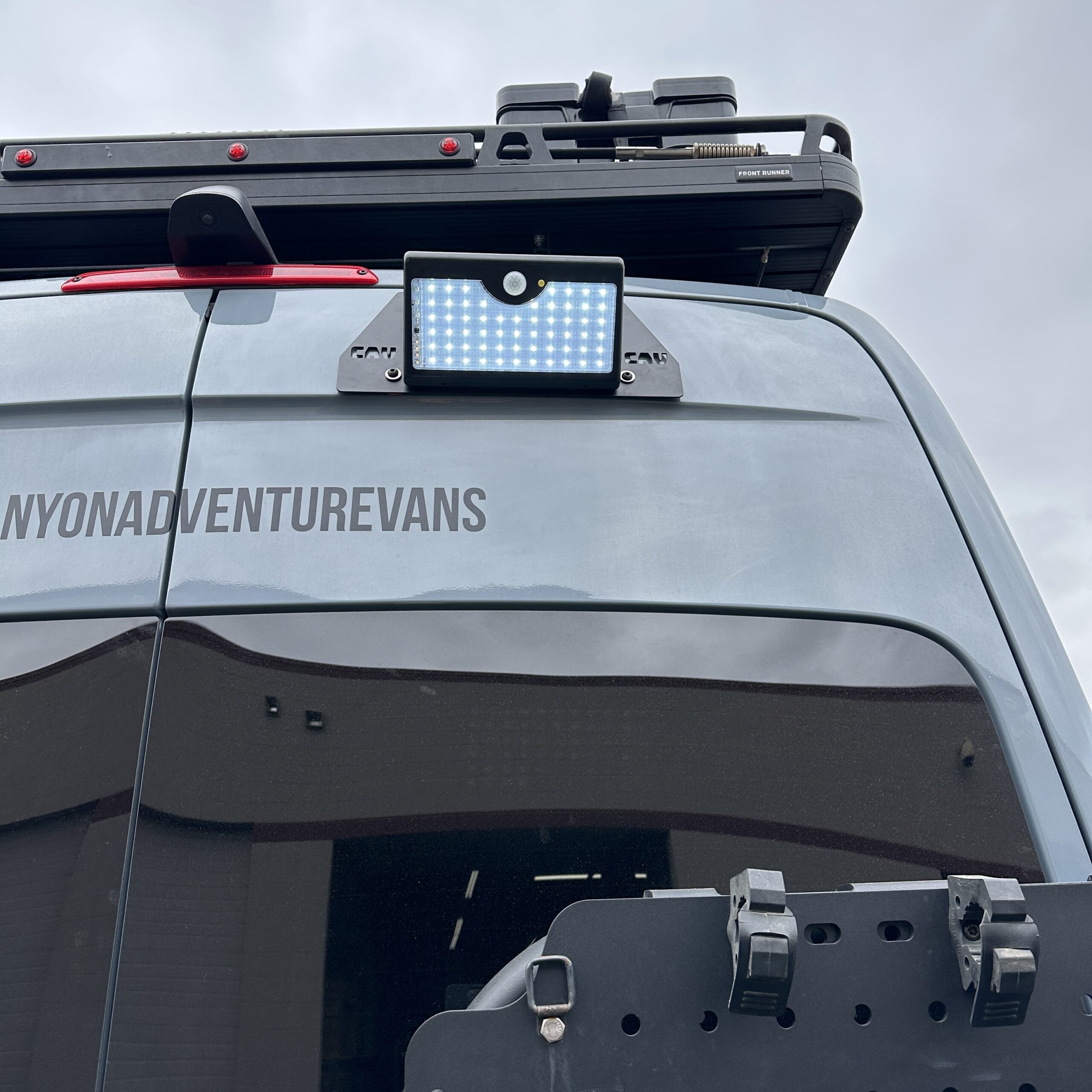 LED flood light mounted on rear of adventure van with roof rack under cloudy sky