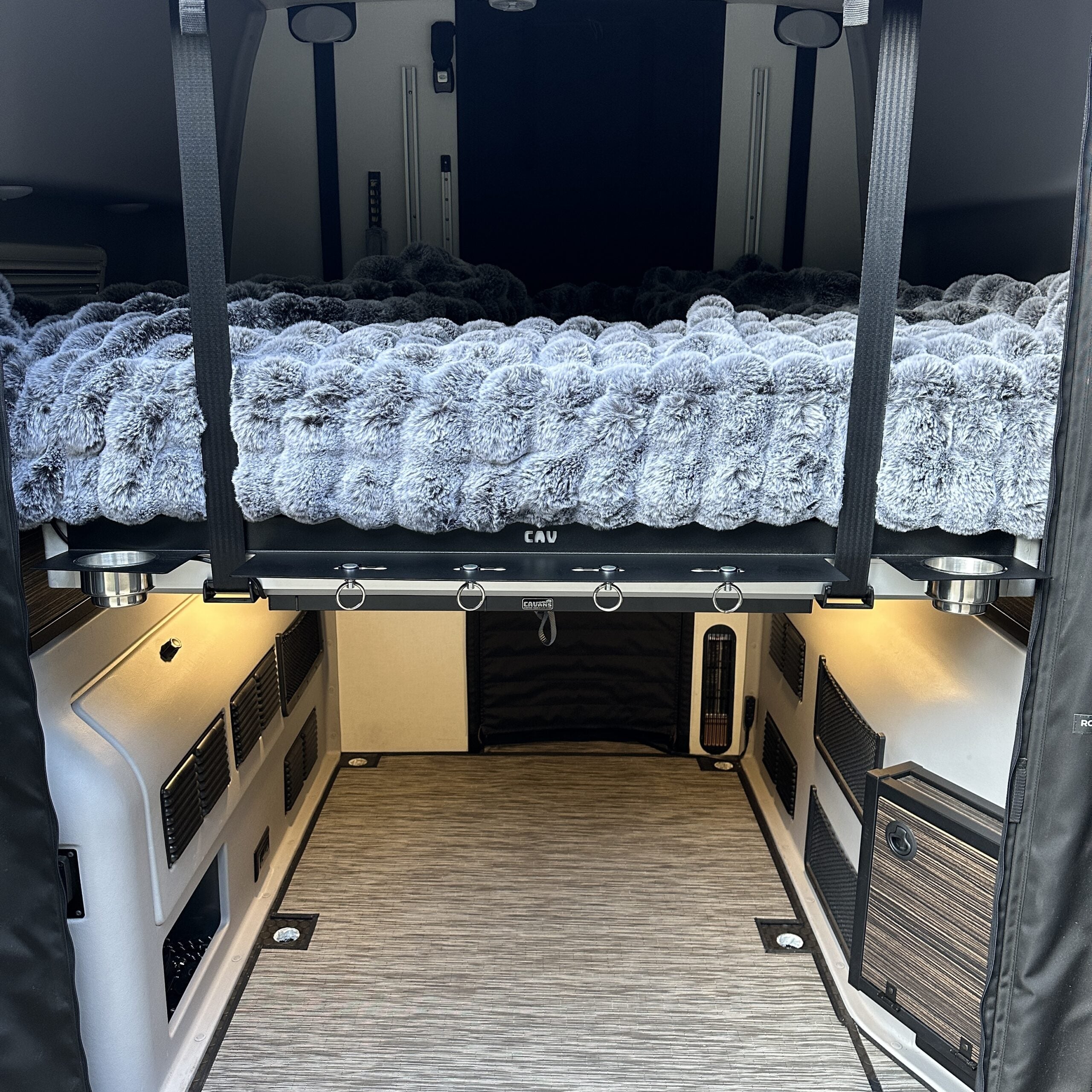 Interior of an overlanding camper with a suspended bed platform and plush bedding