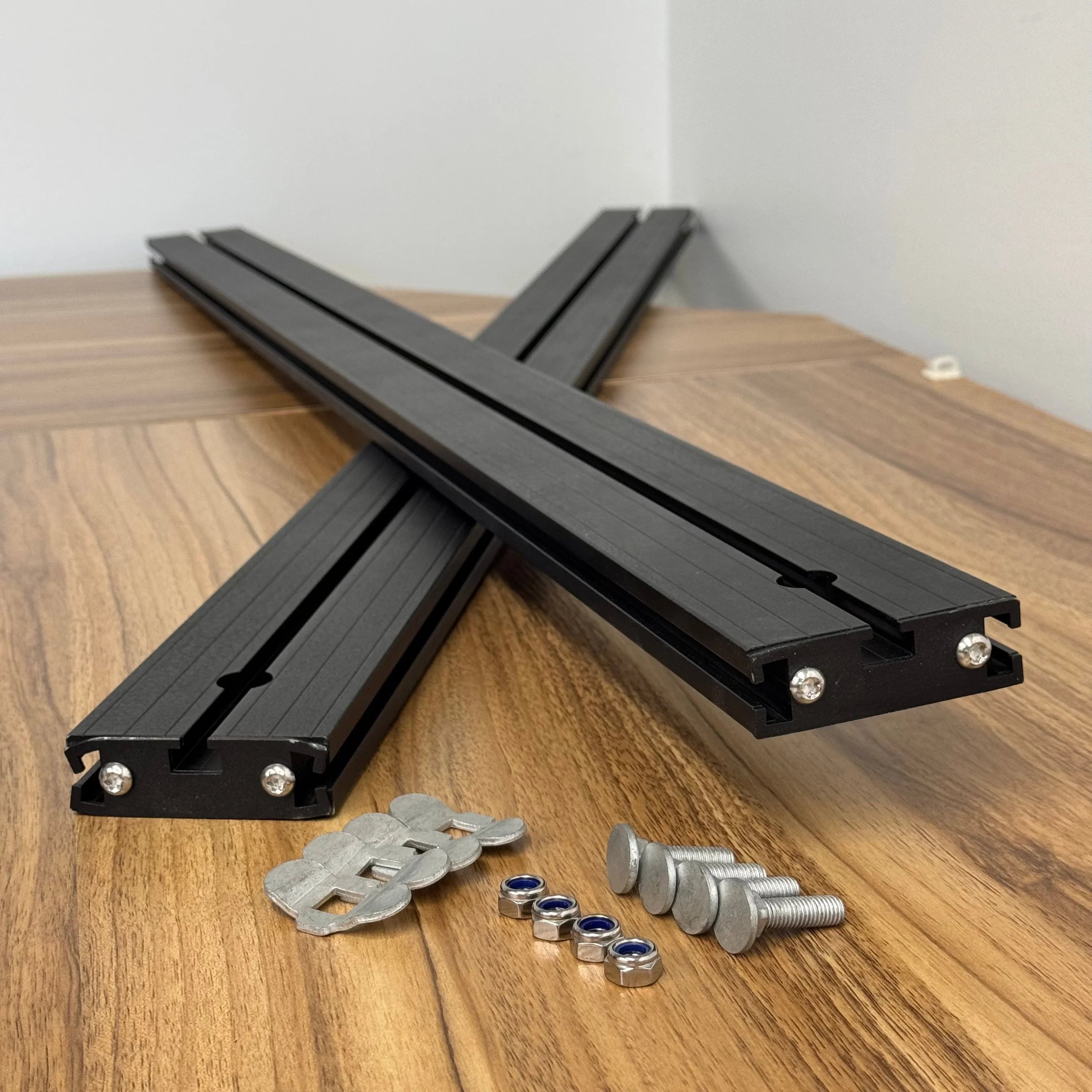 Black aluminum crossbars with mounting hardware for vehicle roof racks on wood table