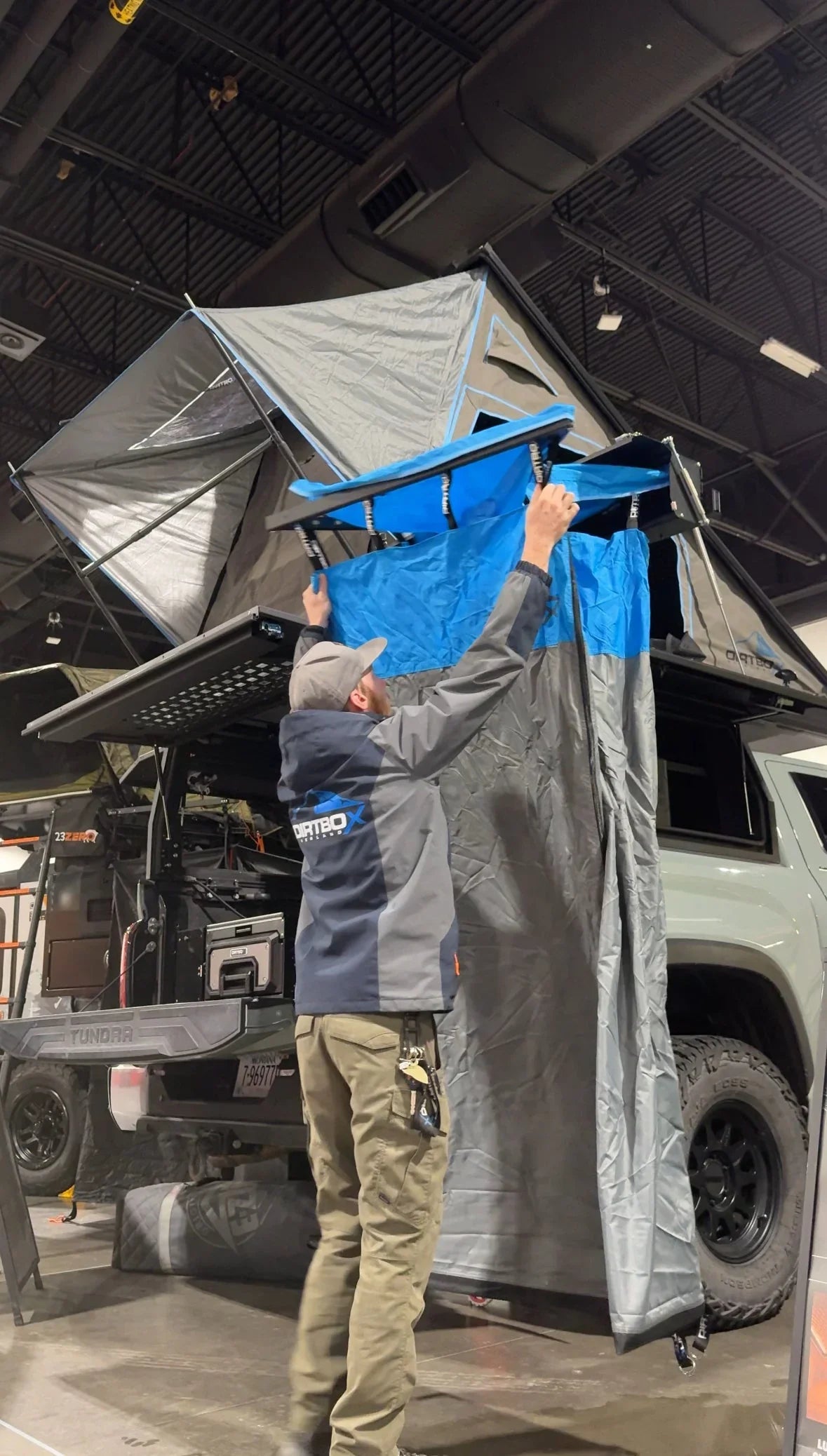 Man setting up overland rooftop tent and awning on Toyota Tundra at indoor expo